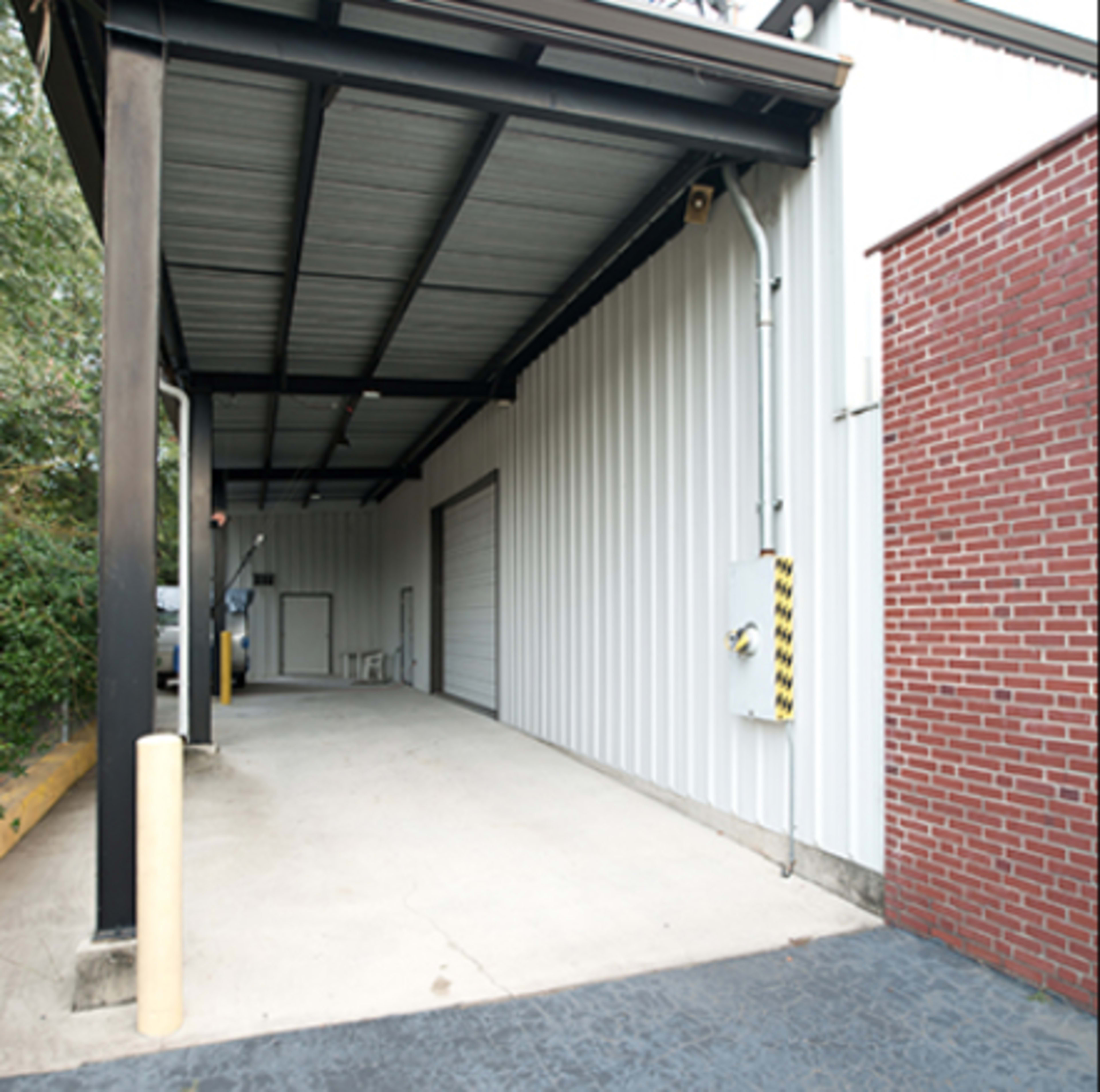 A covered loading area with a metal roof and a cement floor, adjacent to a brick wall.