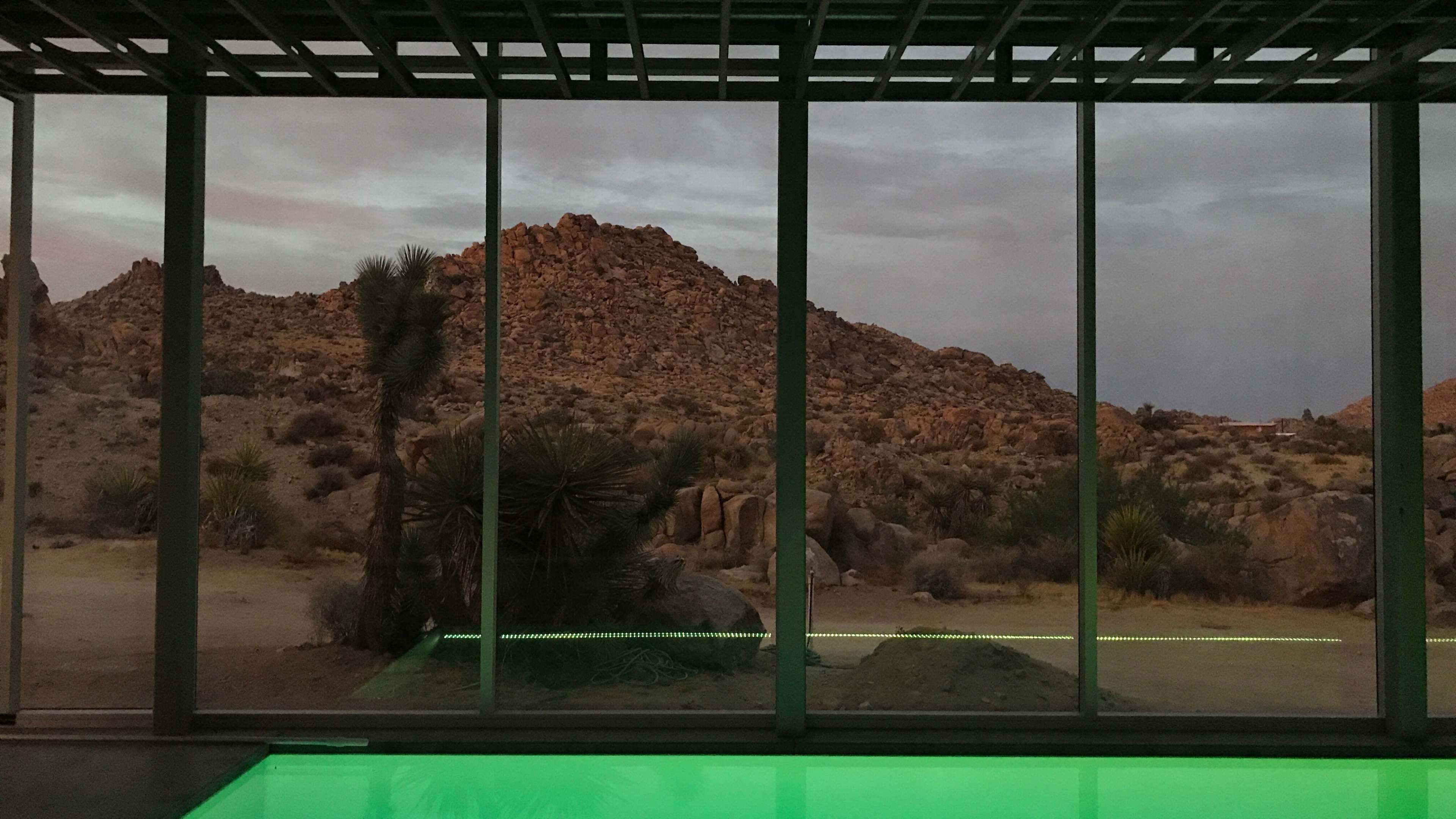 A modern glass structure overlooks a rocky, desert landscape during dusk.