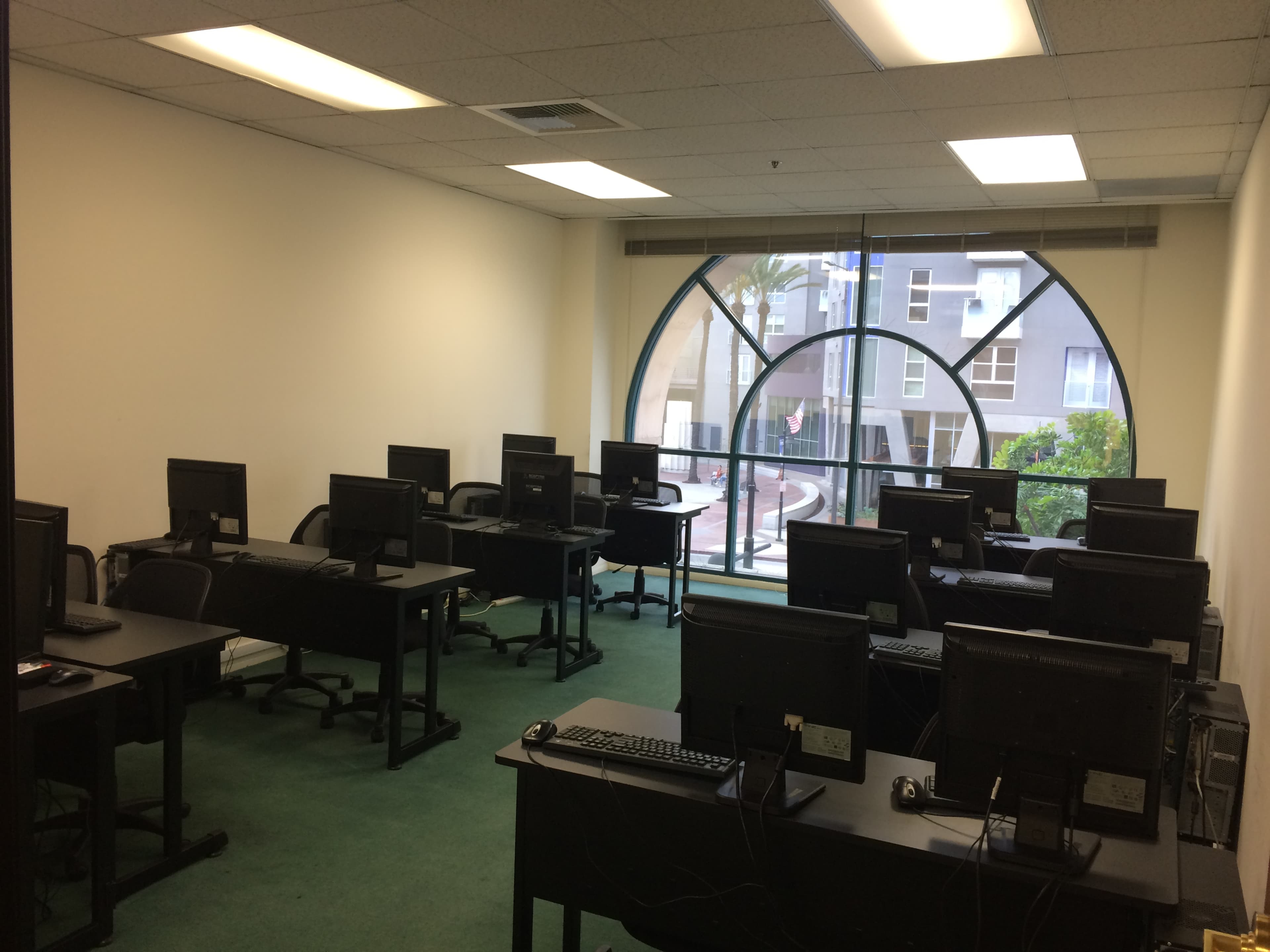 An empty office space with several computer desks arranged in rows, facing a large window with a circular design.