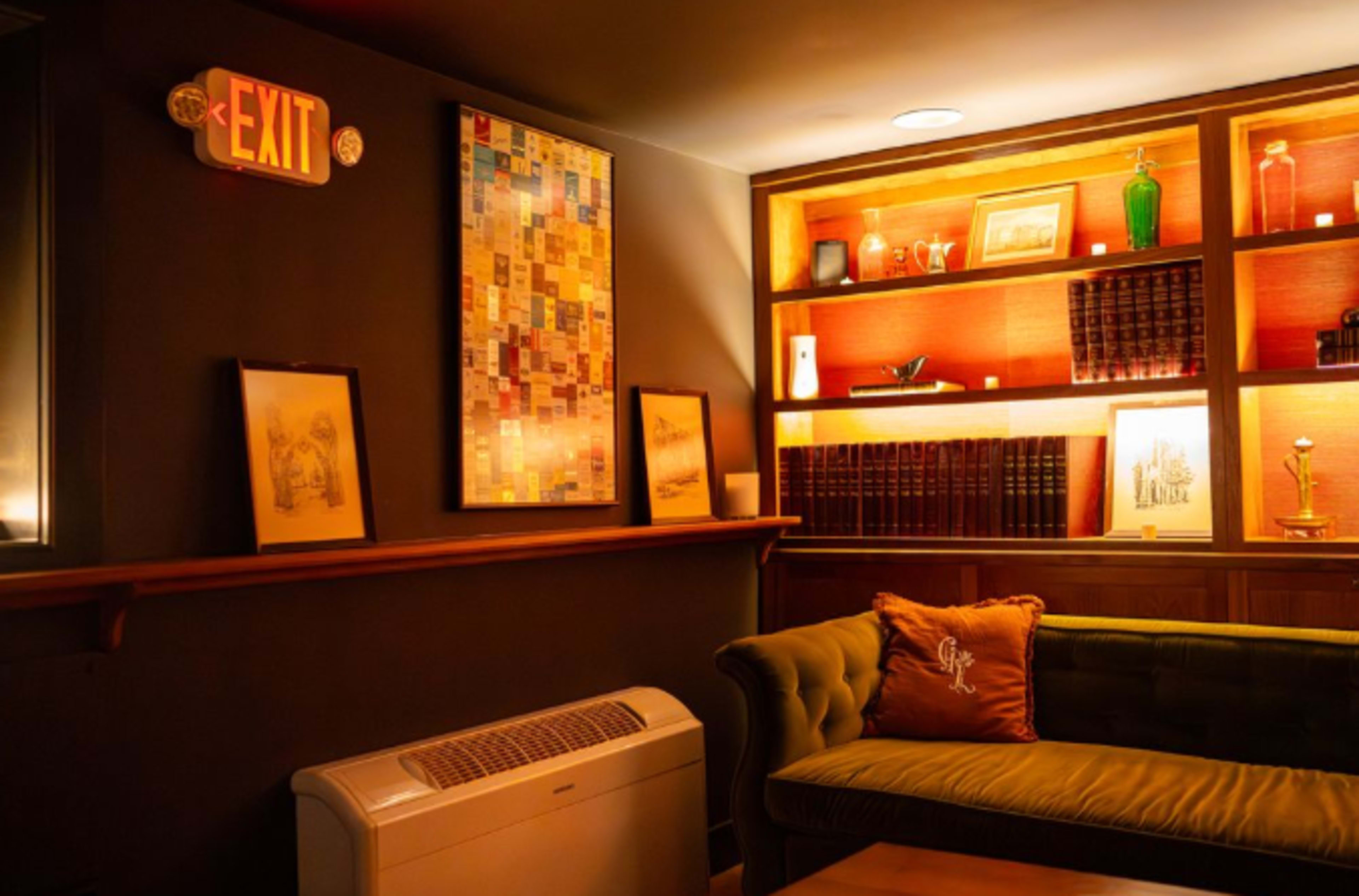 The image shows a cozy room with a green sofa, framed artwork on the walls, and a bookshelf illuminated by warm lighting.