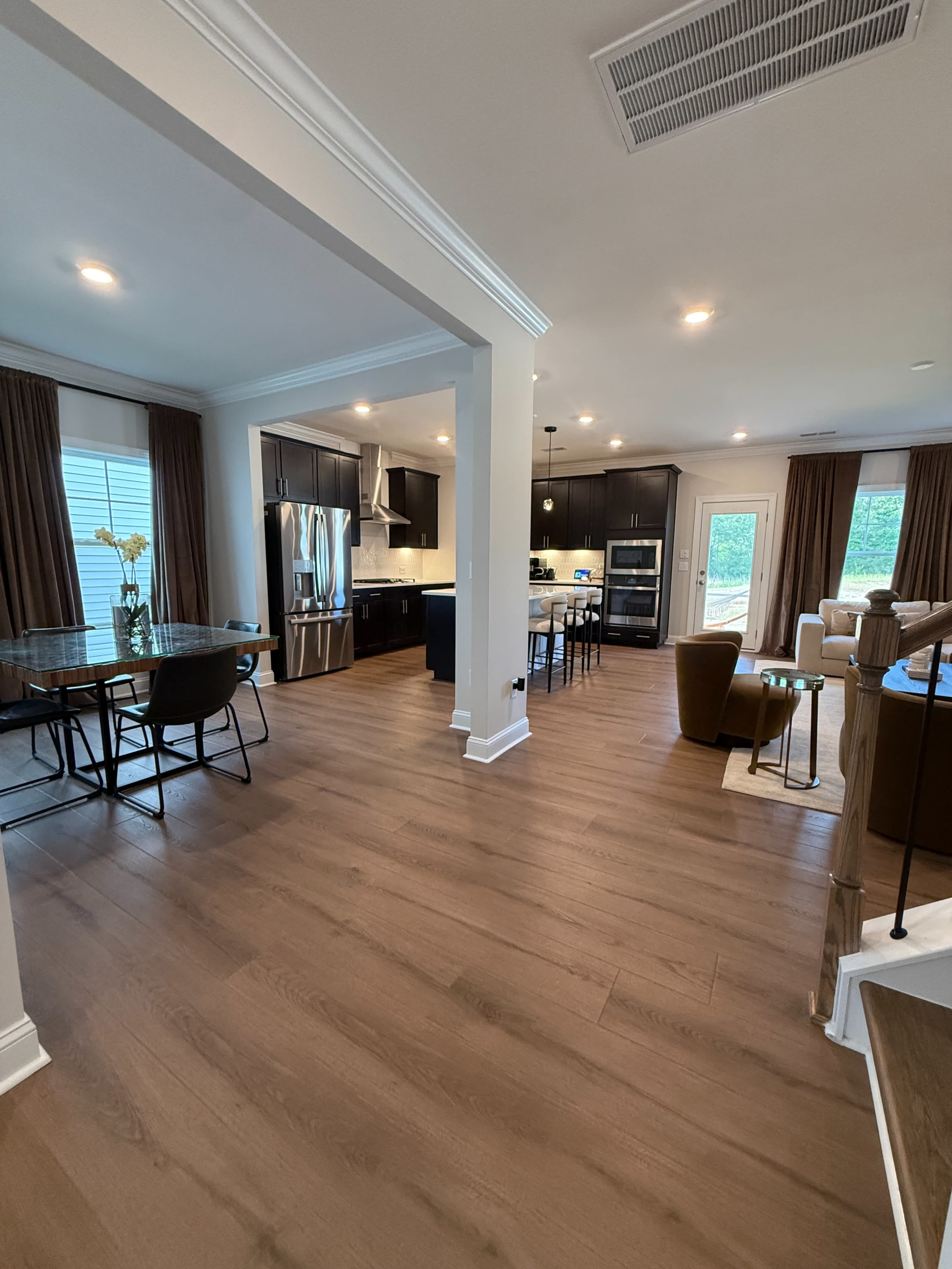The image shows a spacious interior with a dining area, kitchen, and living room featuring hardwood floors and modern furnishings.