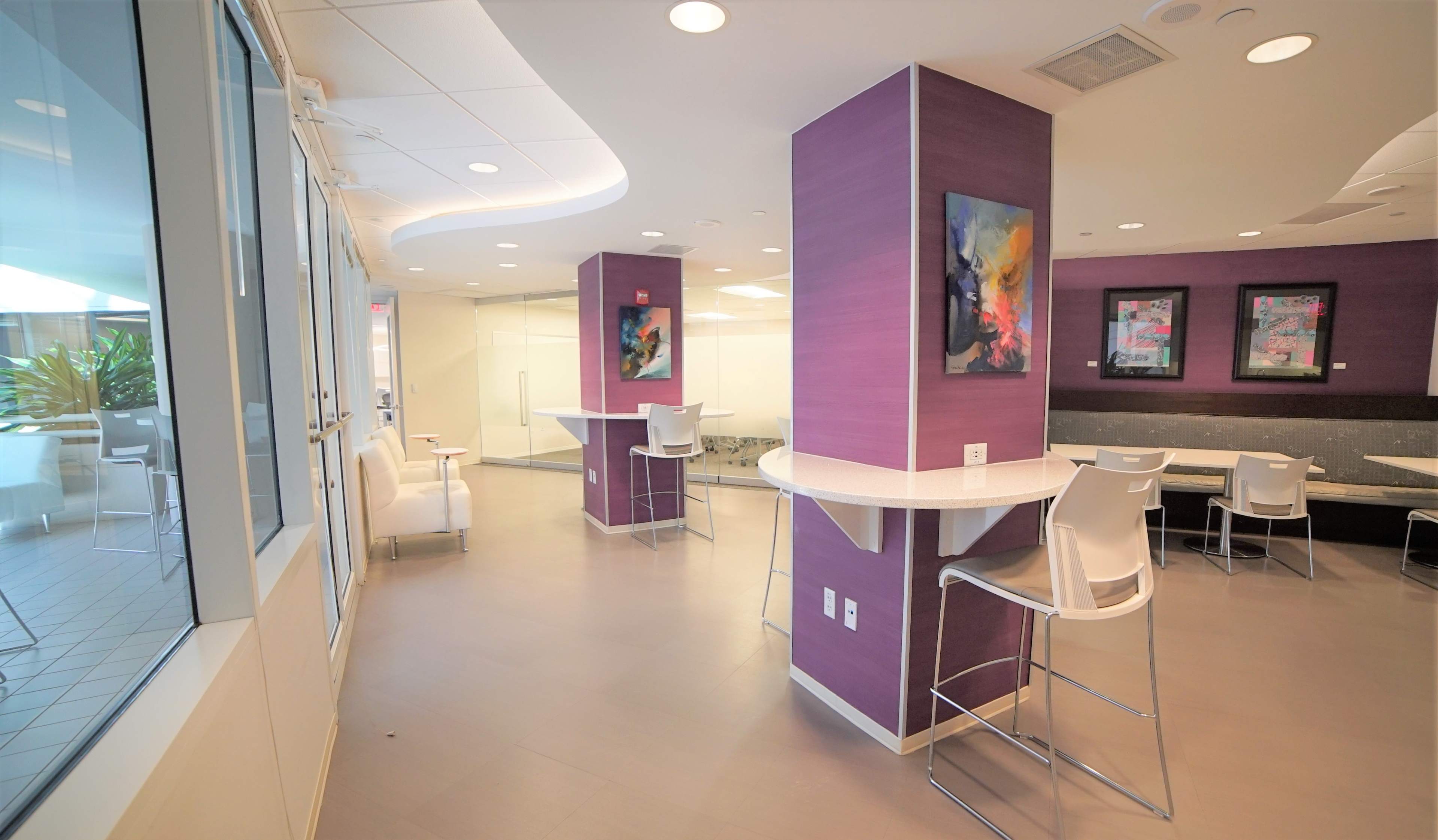 A modern, open lounge area with purple accent walls, high-top tables, and contemporary chairs.