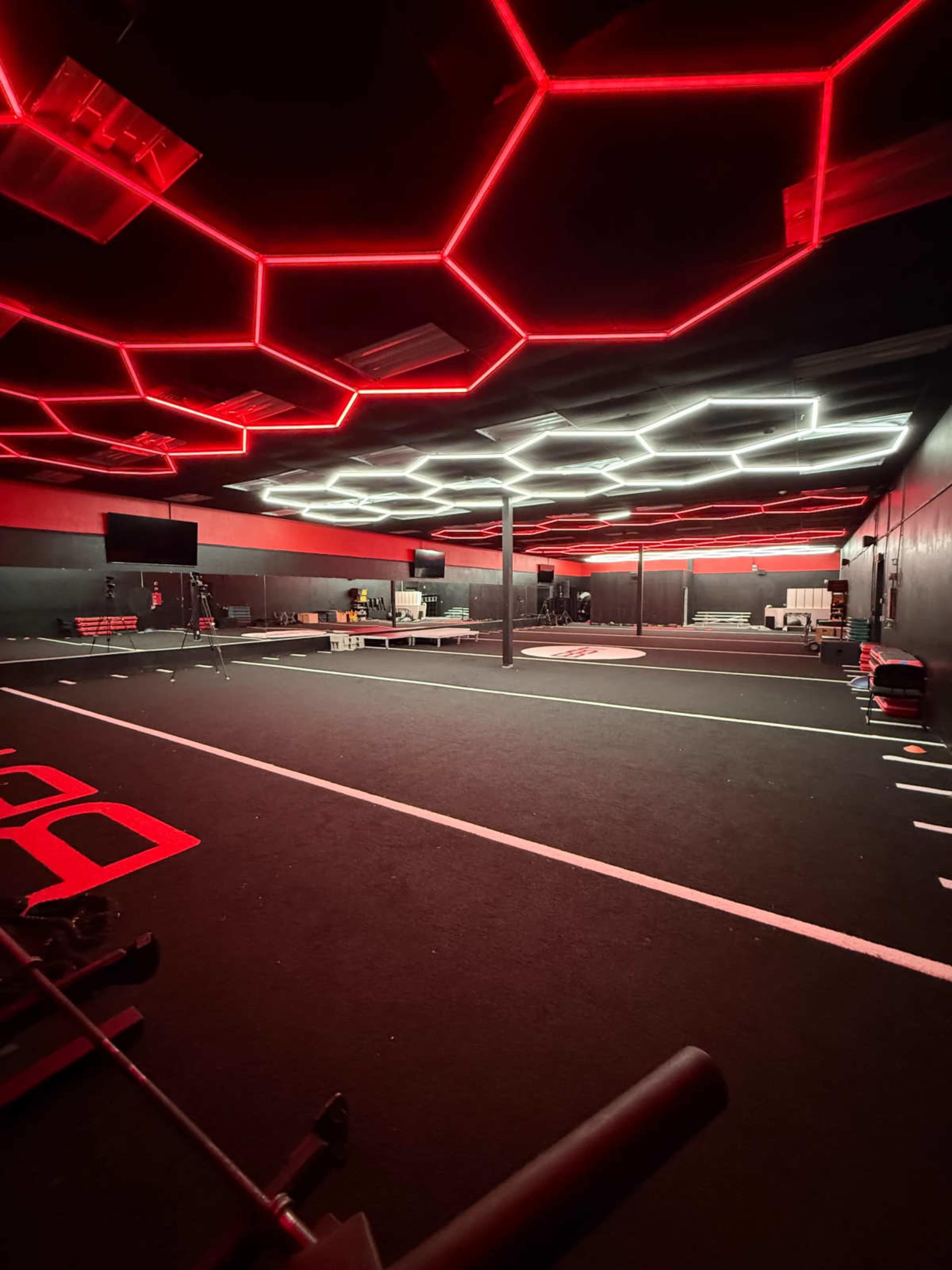 The image depicts a fitness or training facility with a dark floor, illuminated by red and white hexagon-shaped ceiling lights and various workout equipment scattered throughout the space.