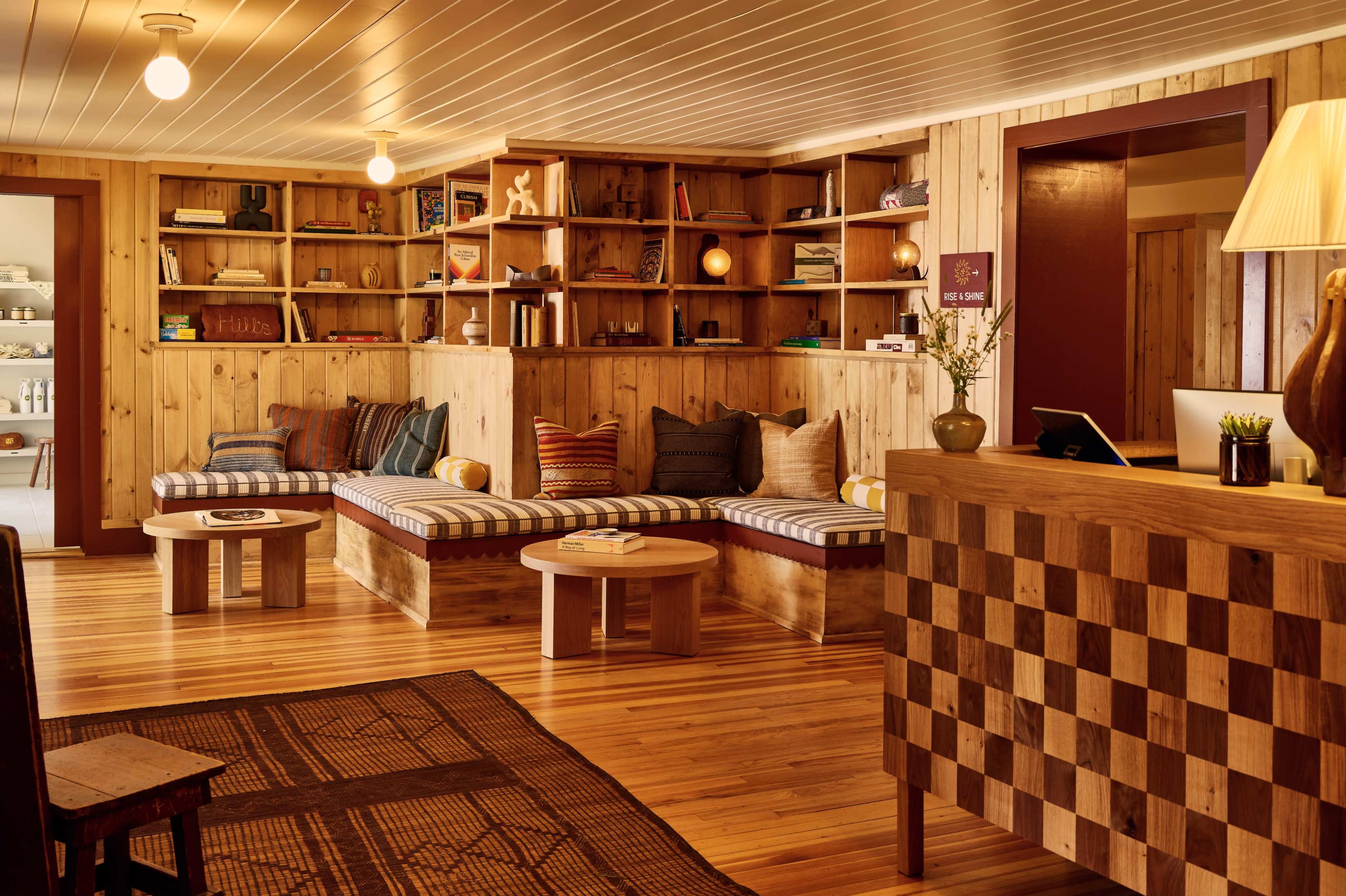 A cozy room with wooden walls and shelves filled with books, featuring low seating and a reception desk.