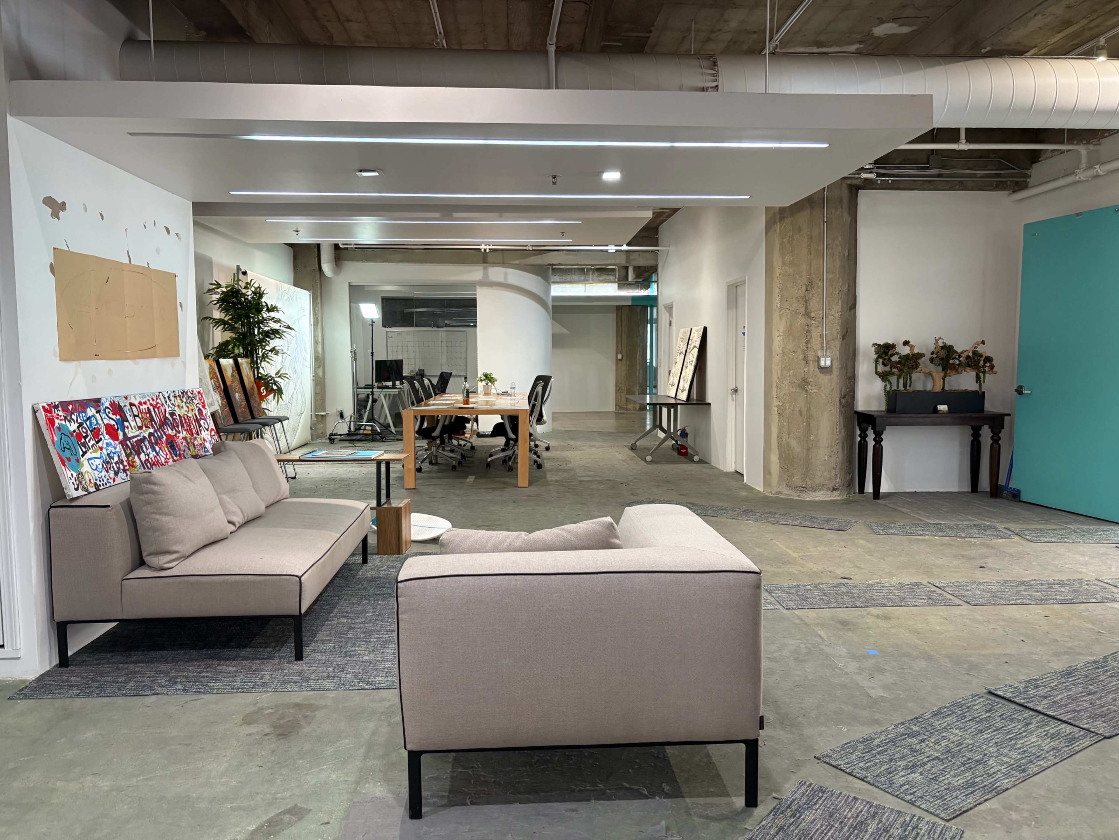 The image shows a modern office space with a couch in the foreground, a wooden table and chairs in the background, and various decorations on the walls.