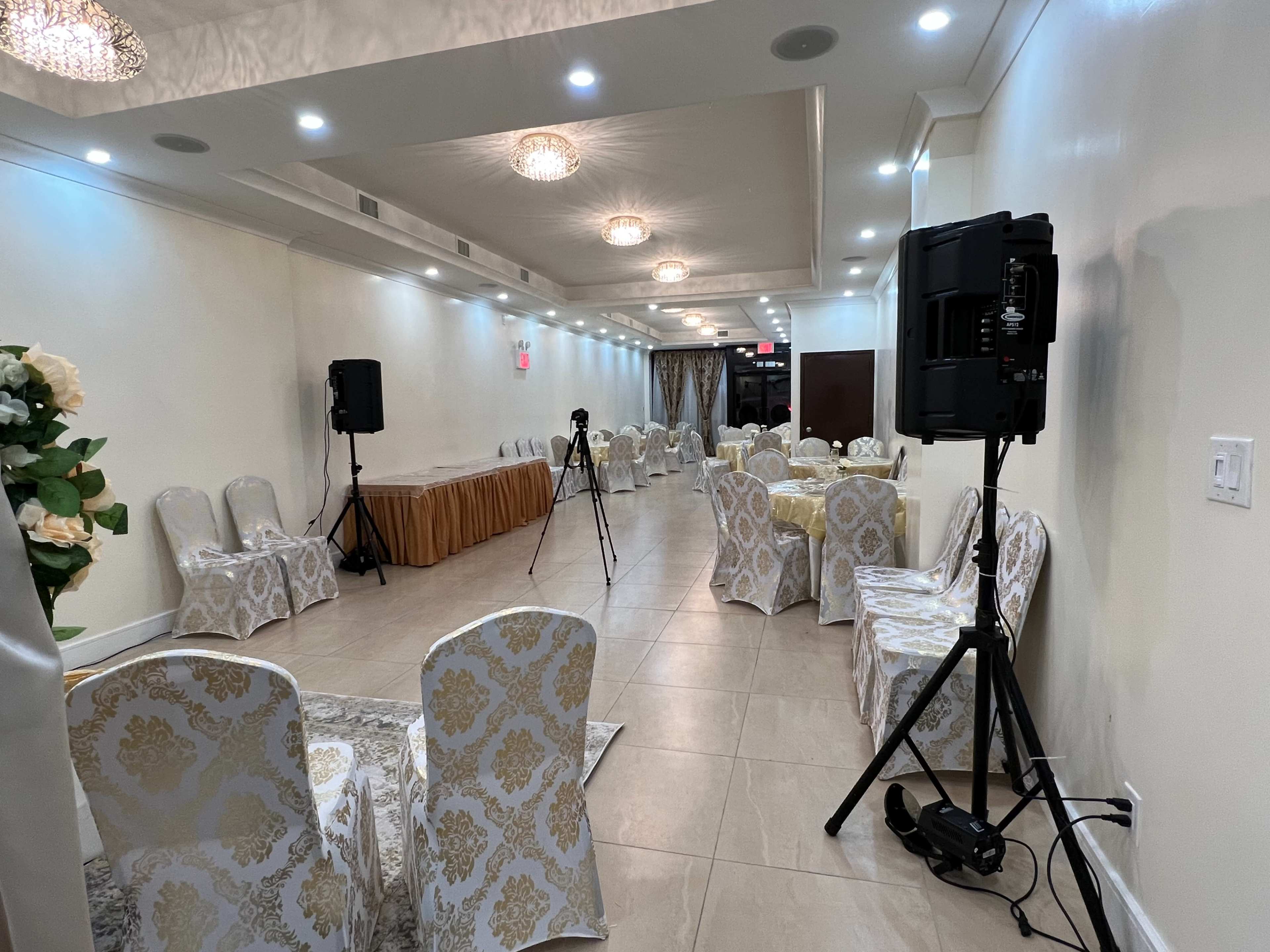 A banquet hall with decorative chairs and tables set up, along with sound equipment and cameras positioned in the corners.