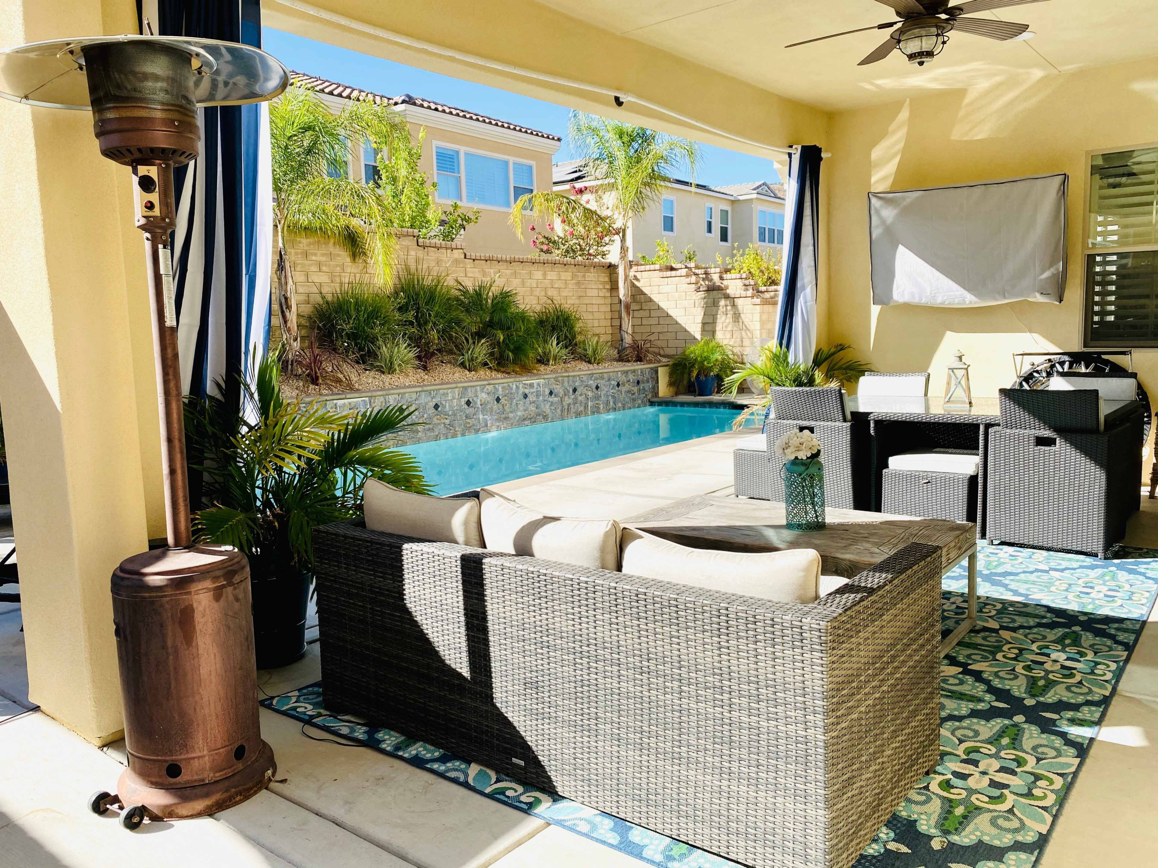 The image shows a patio area with a pool in the background, featuring outdoor furniture and a heater.