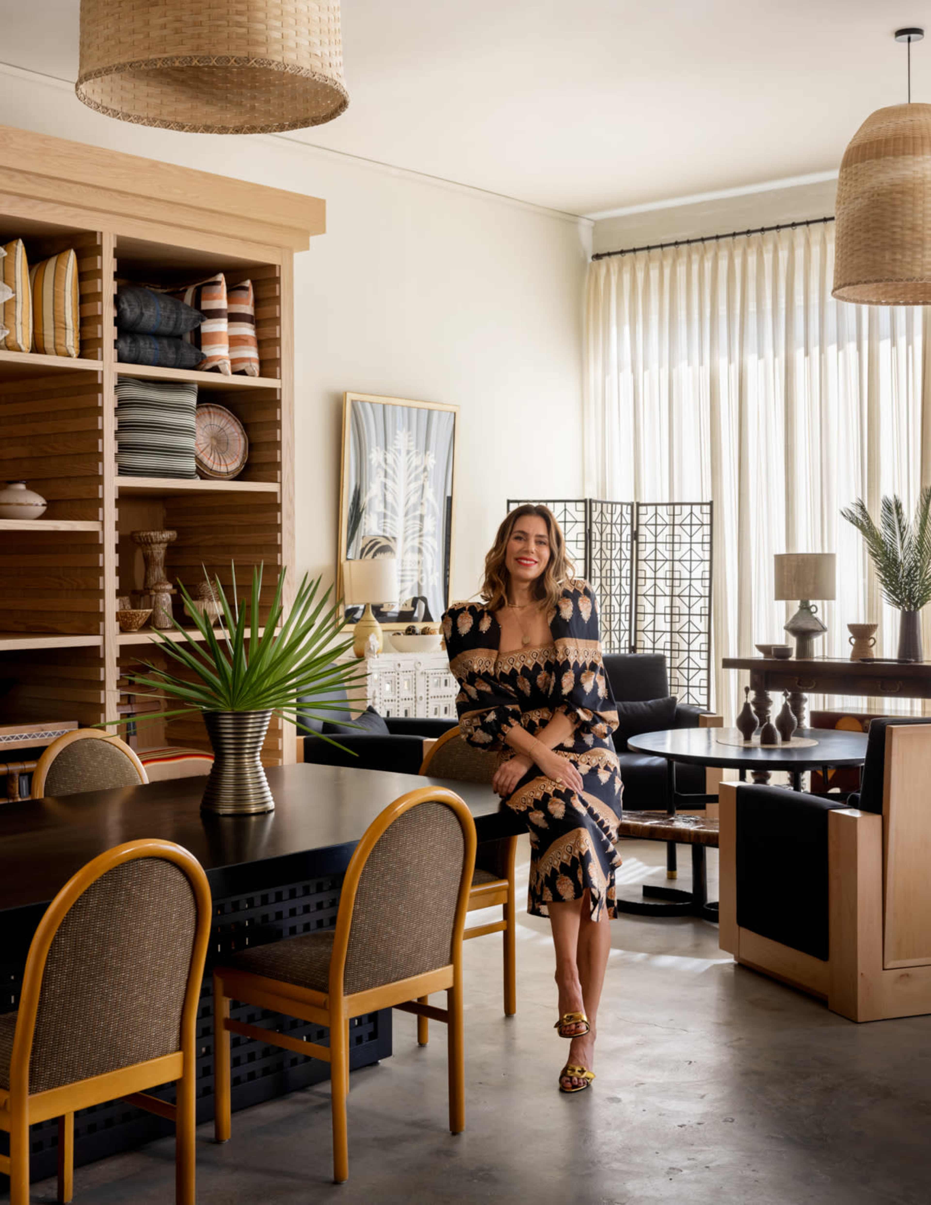 A woman in a patterned dress stands in a modern interior space featuring diverse furniture and decor elements.
