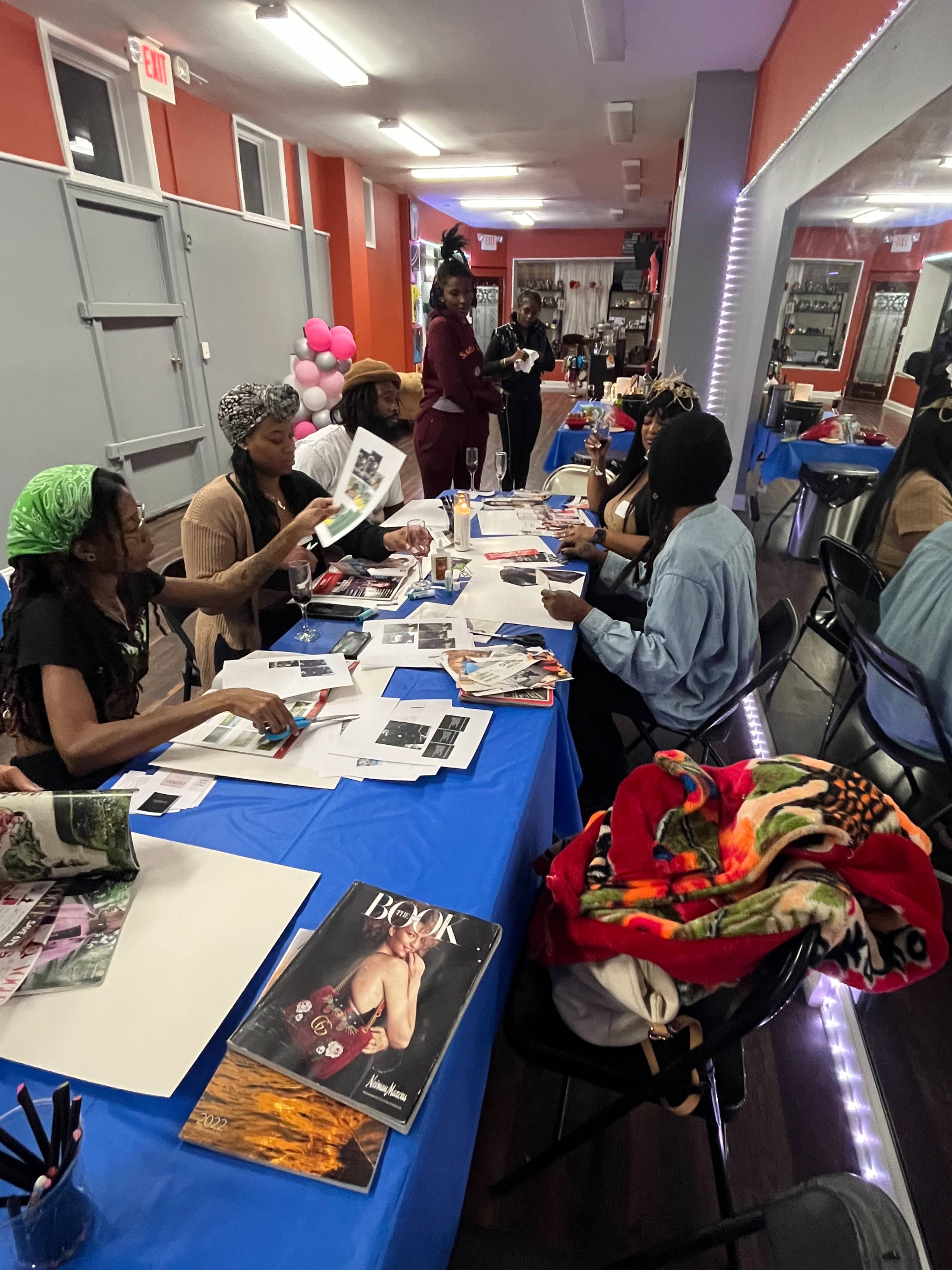 A group of people are seated at a table, working on creative projects with magazines and art supplies in a brightly lit community space.