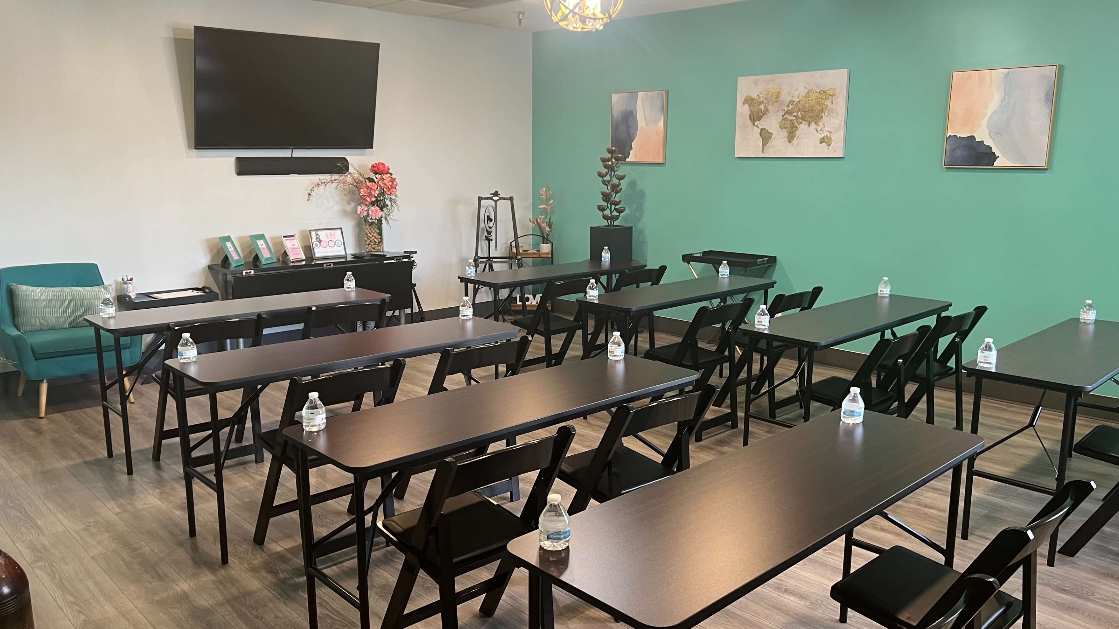 A modern training room with black folding tables arranged in rows, featuring water bottles on each table and a large screen mounted on the wall.
