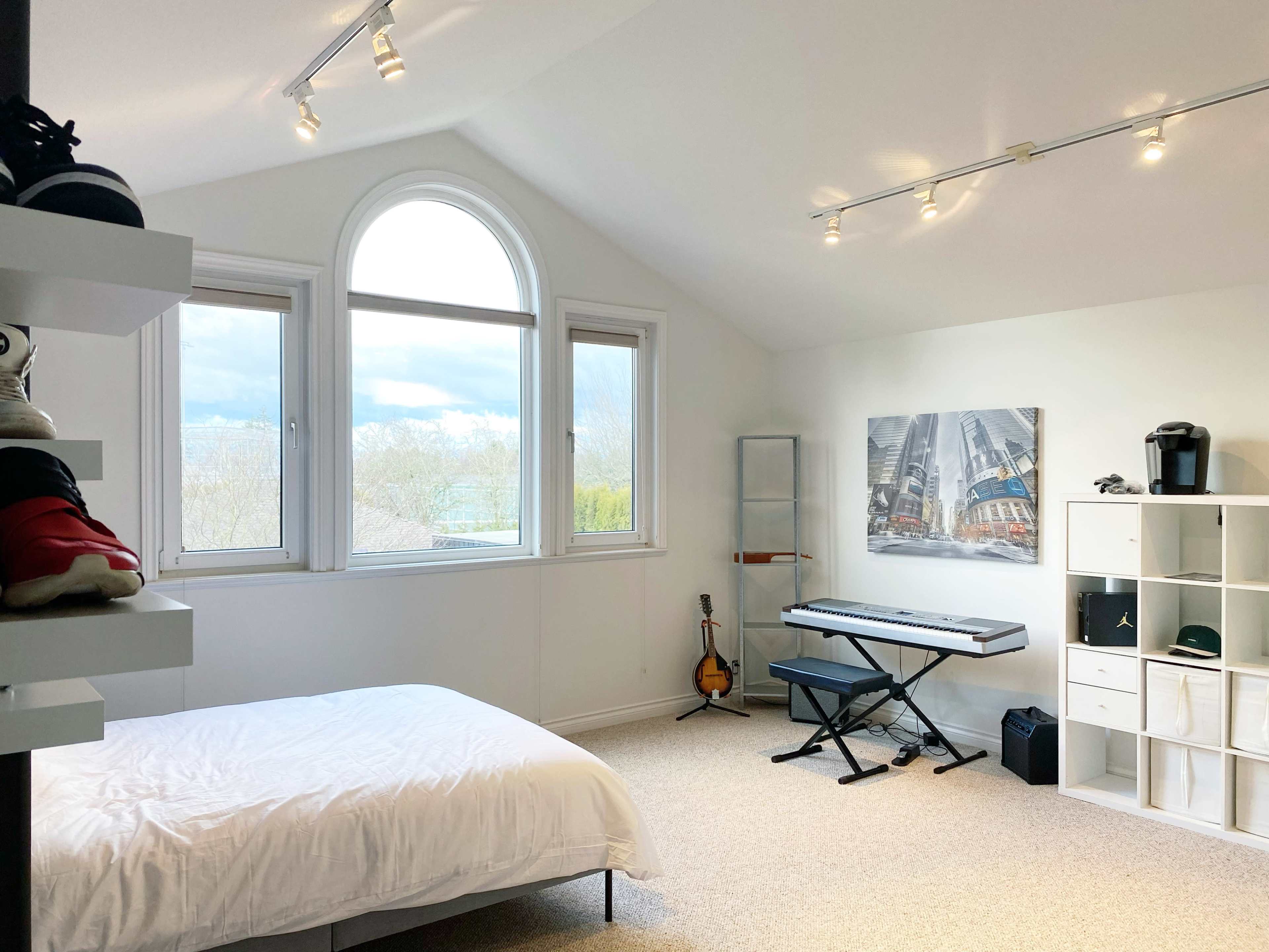 The room features a bed, a keyboard, a guitar, and a window with a curved top, all arranged around light-colored walls with a modern decor.