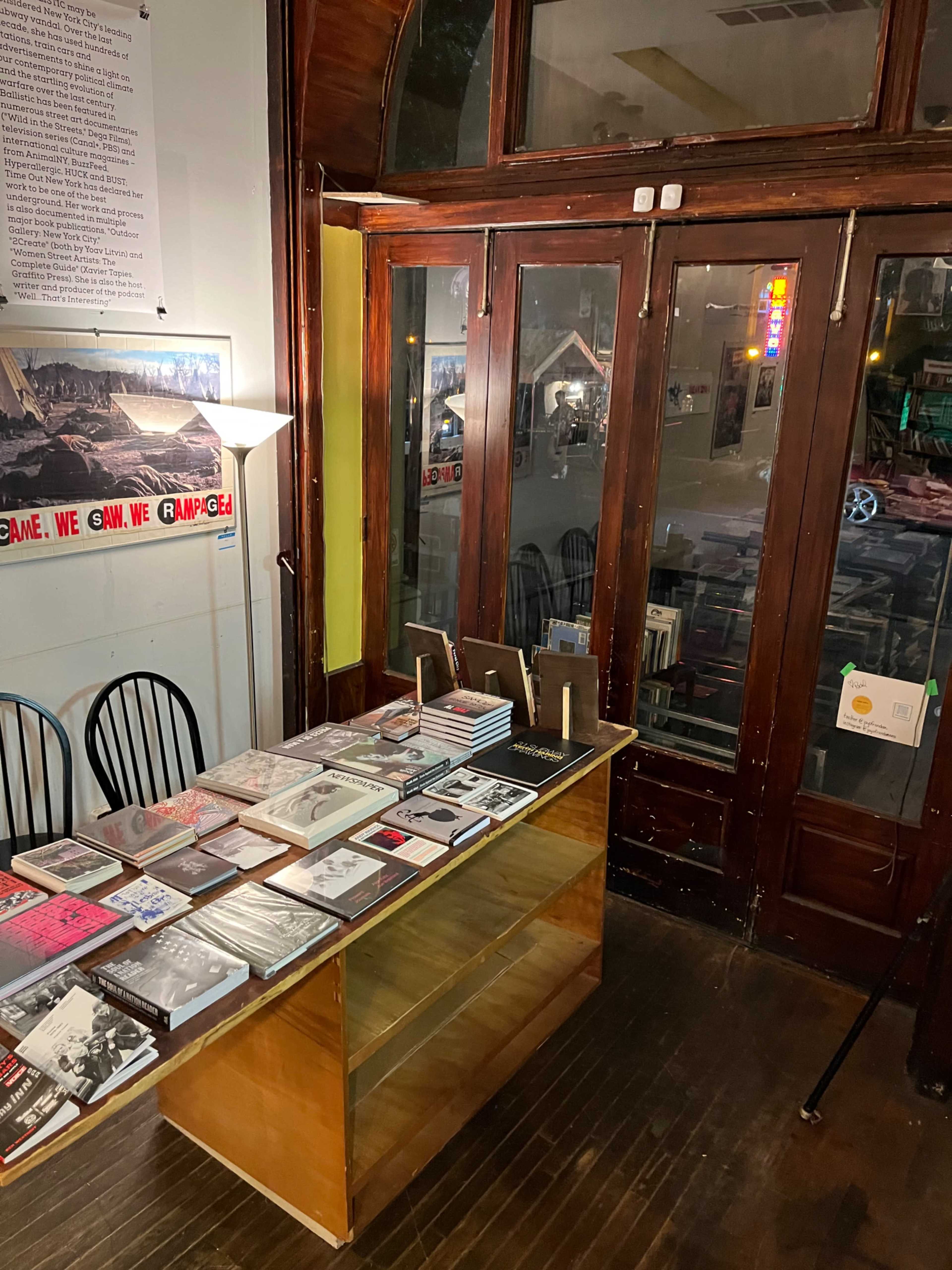 A wooden table displays various books in front of a glass door with a reflection of a street scene.