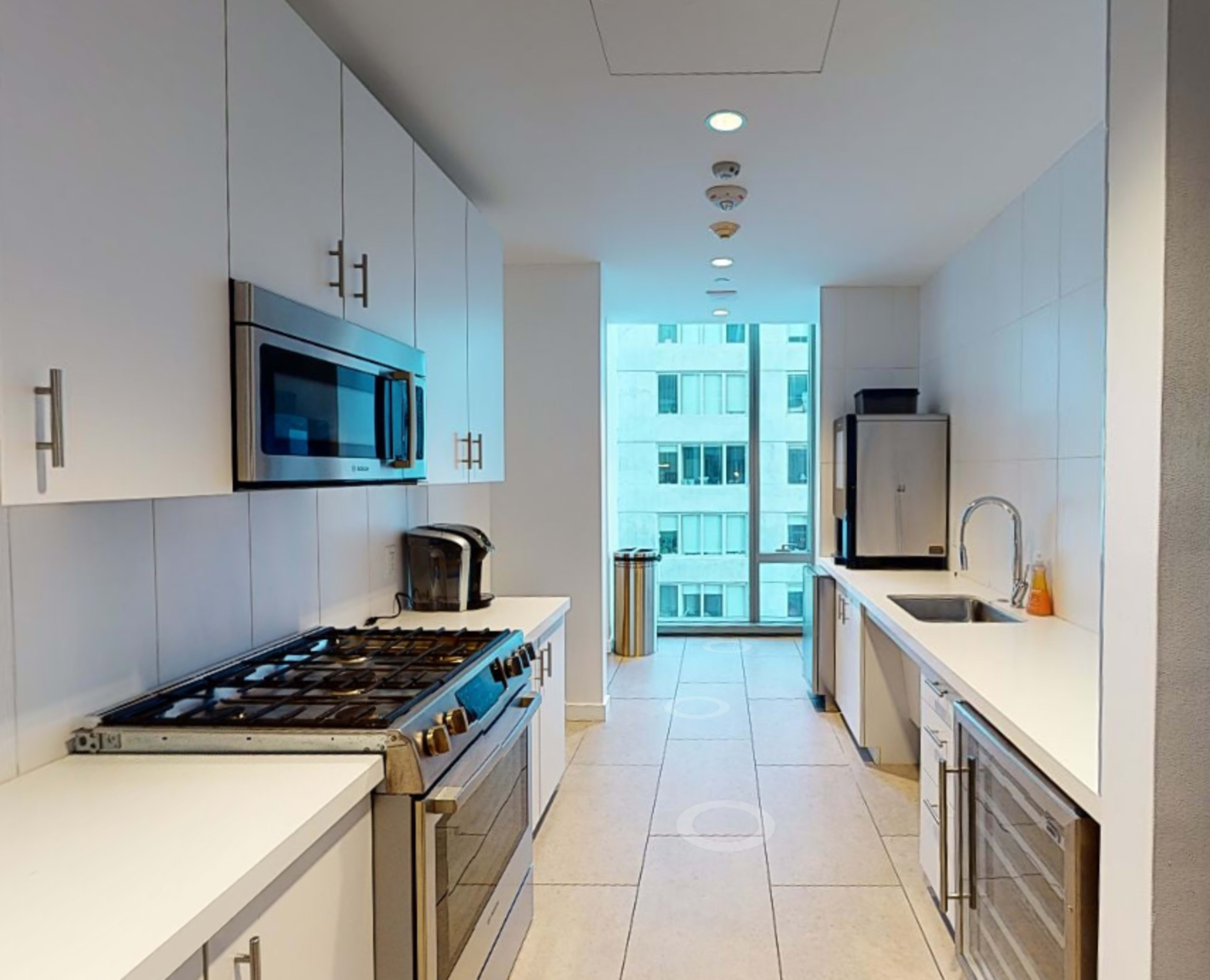 A modern kitchen features white cabinets, stainless steel appliances, and a large window overlooking a cityscape.