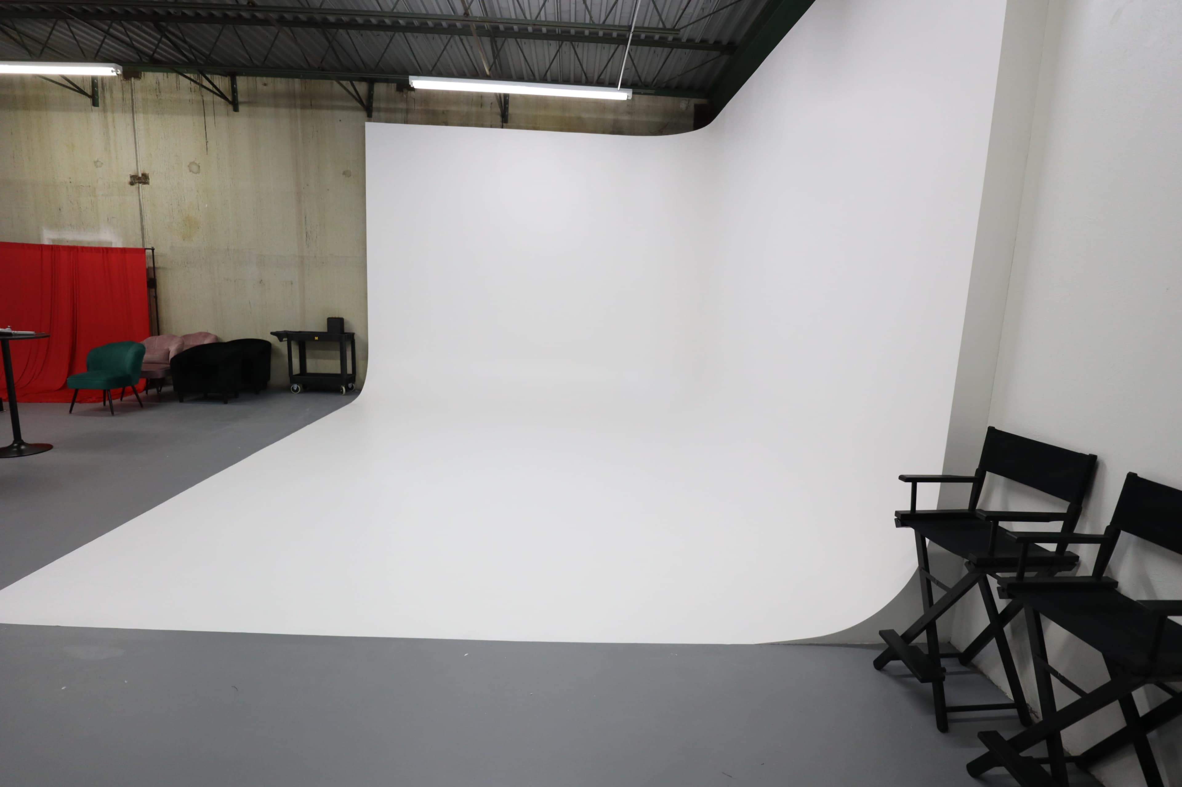 A clean, empty photo studio features a seamless white backdrop and a few chairs set against a gray floor.