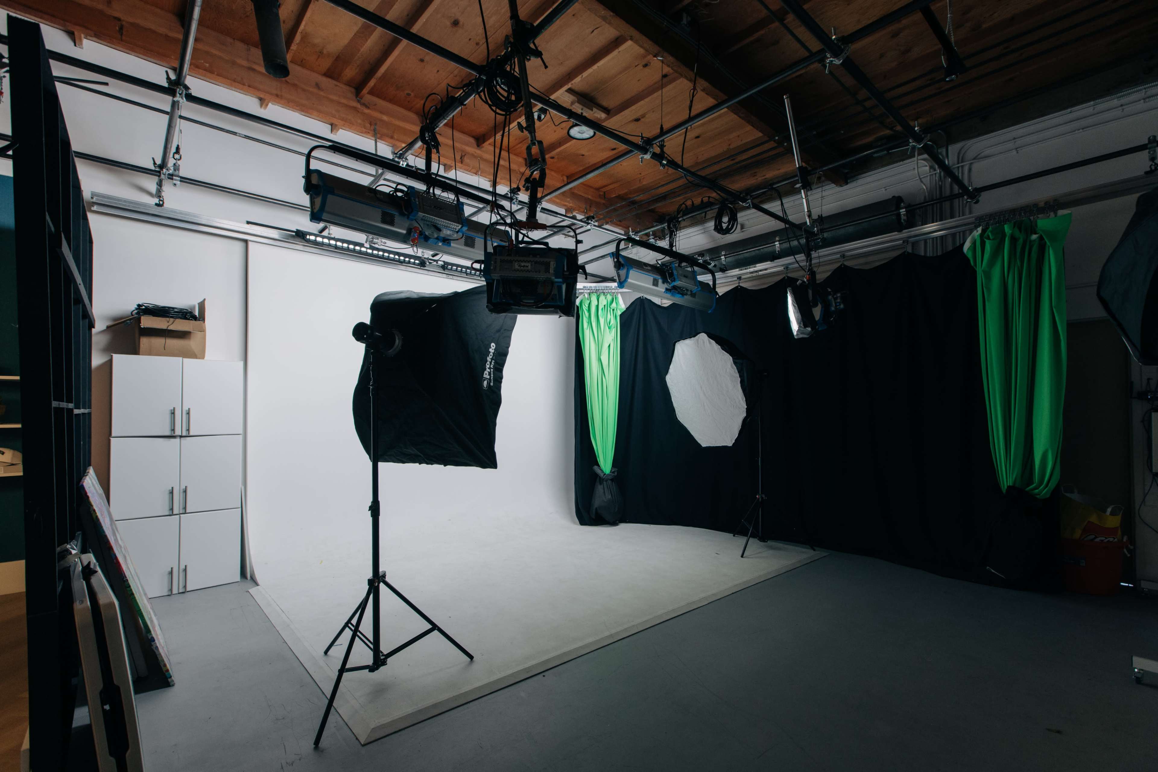 The image shows a photography studio with a backdrop, lighting equipment, and green curtains.