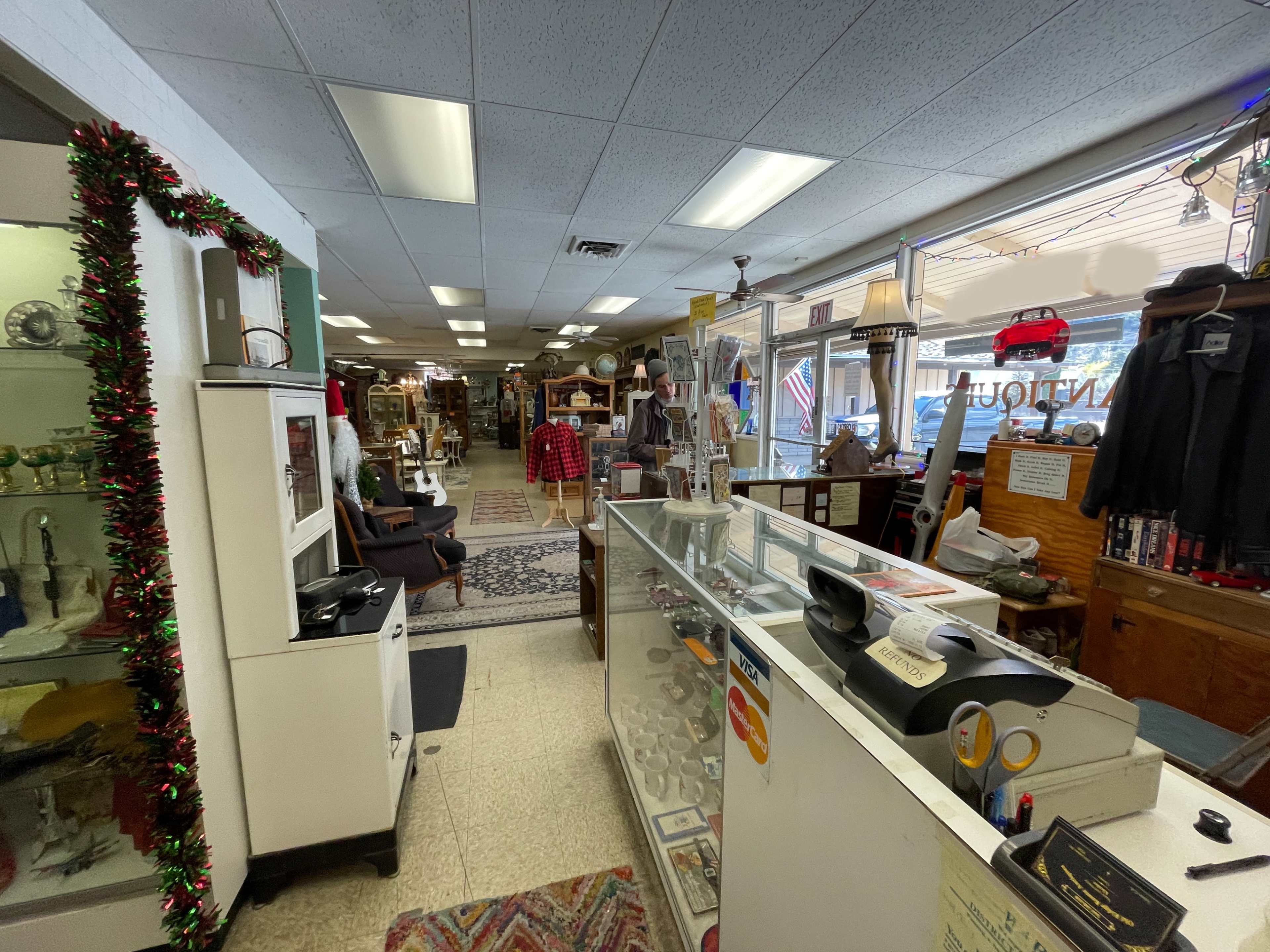 The image shows the interior of an antique shop featuring a display counter and various items arranged on shelves and tables throughout the space.