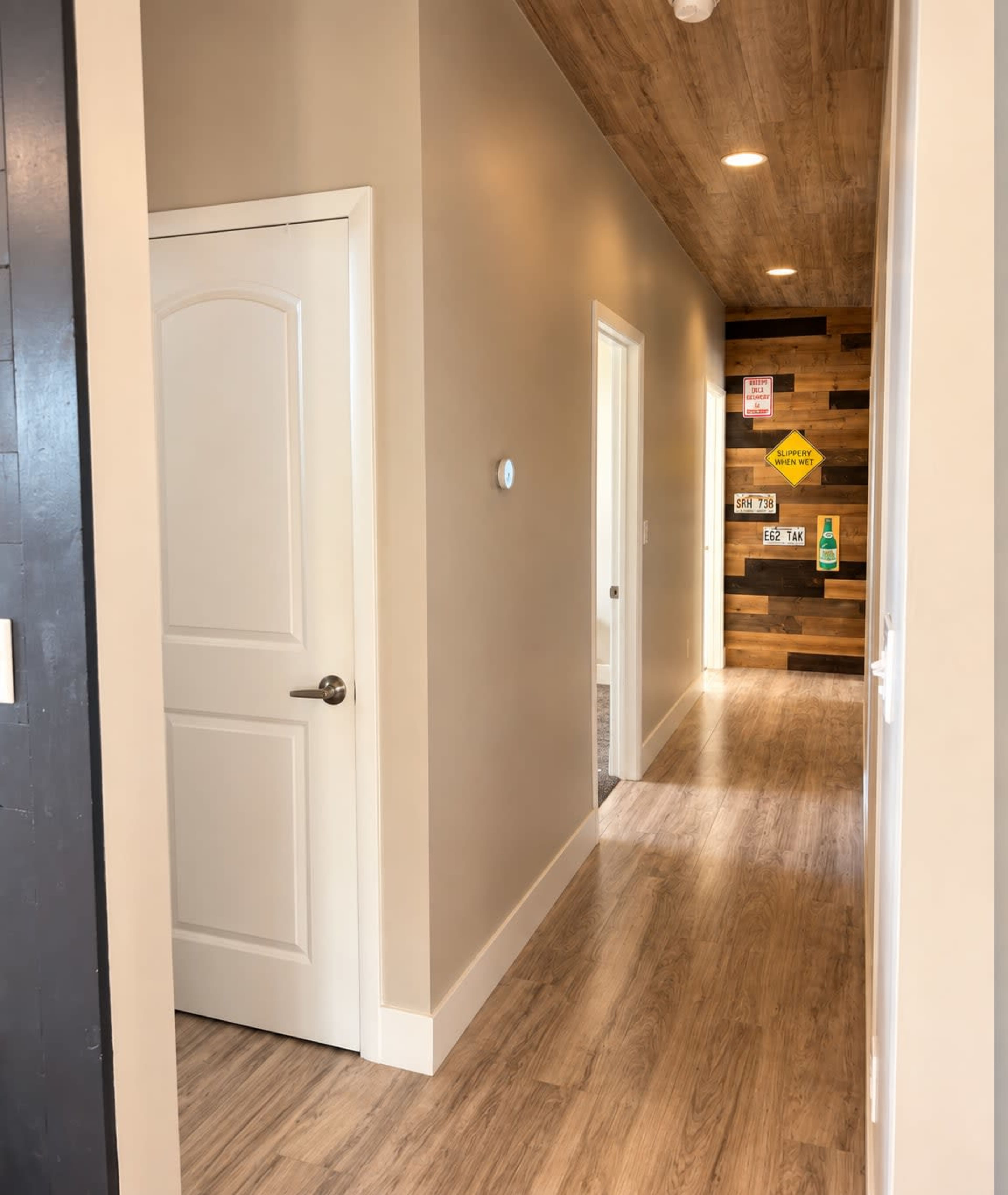 A well-lit hallway features a closed door on the left, with a textured wooden accent wall at the far end and light-colored walls throughout.