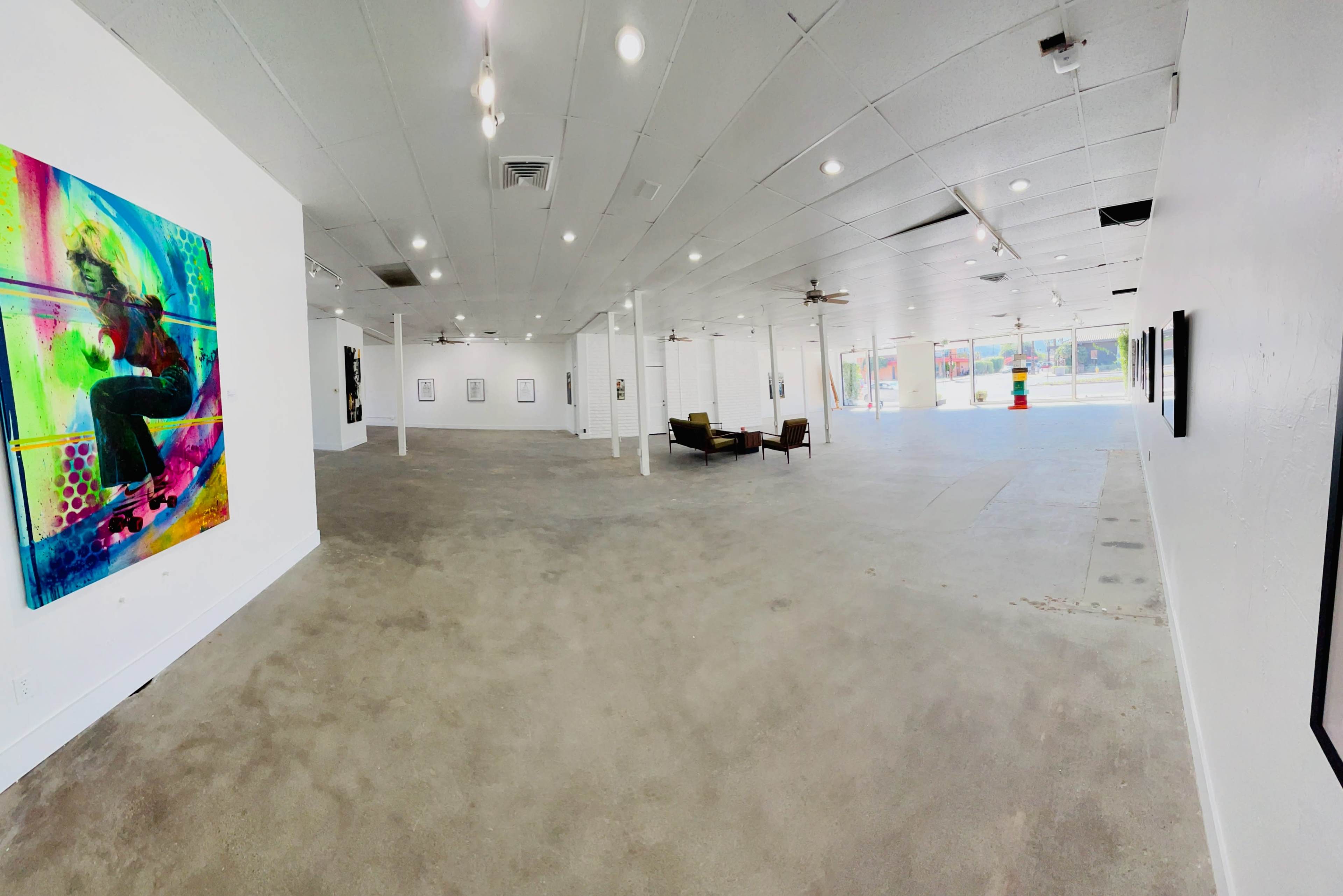 An empty art gallery with white walls, polished concrete floors, and a seating area featuring two chairs.