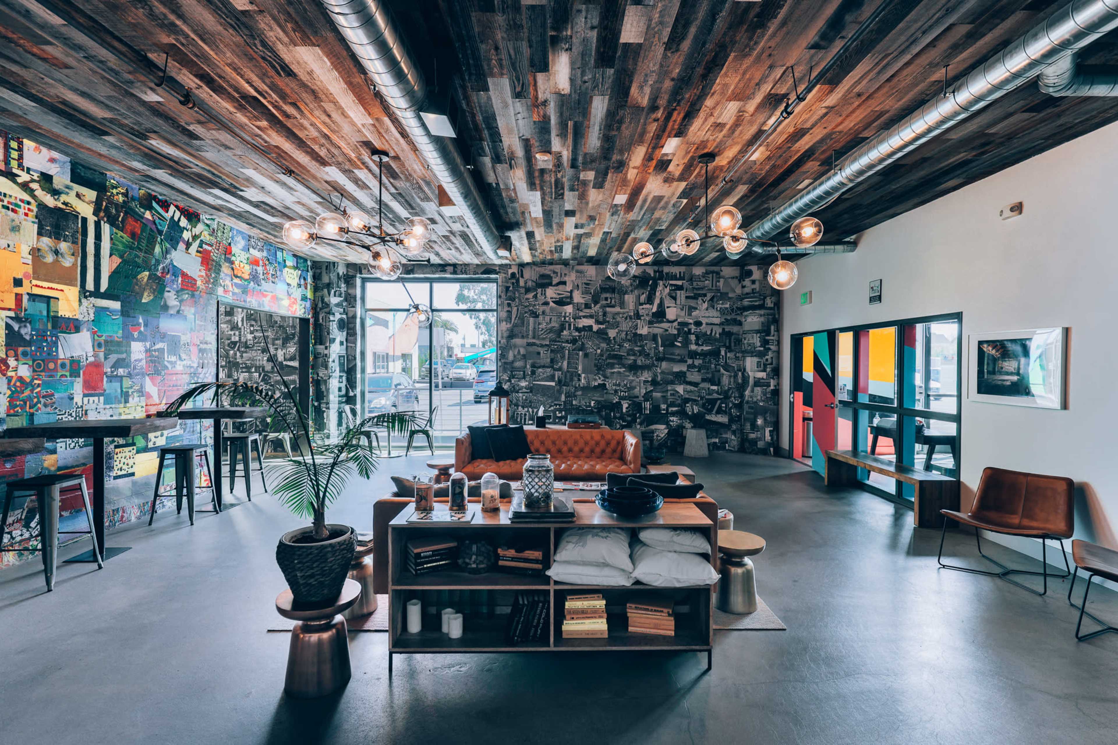 The image shows a modern café interior featuring a wooden ceiling, eclectic wall décor, and a mix of seating options including a leather couch and metal chairs.