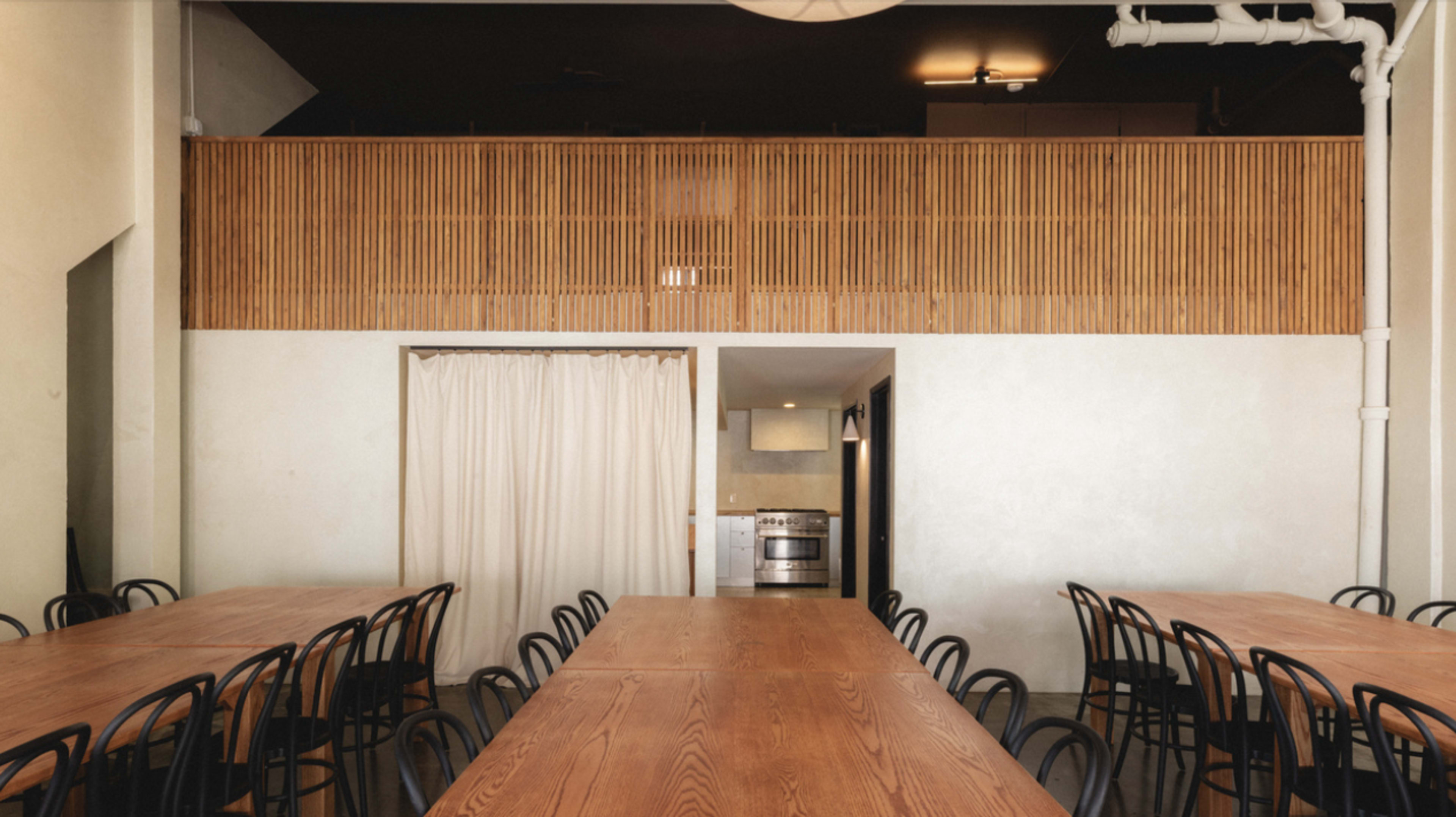 The interior features a spacious dining area with long wooden tables and a bamboo partition that separates the kitchen from the main space.