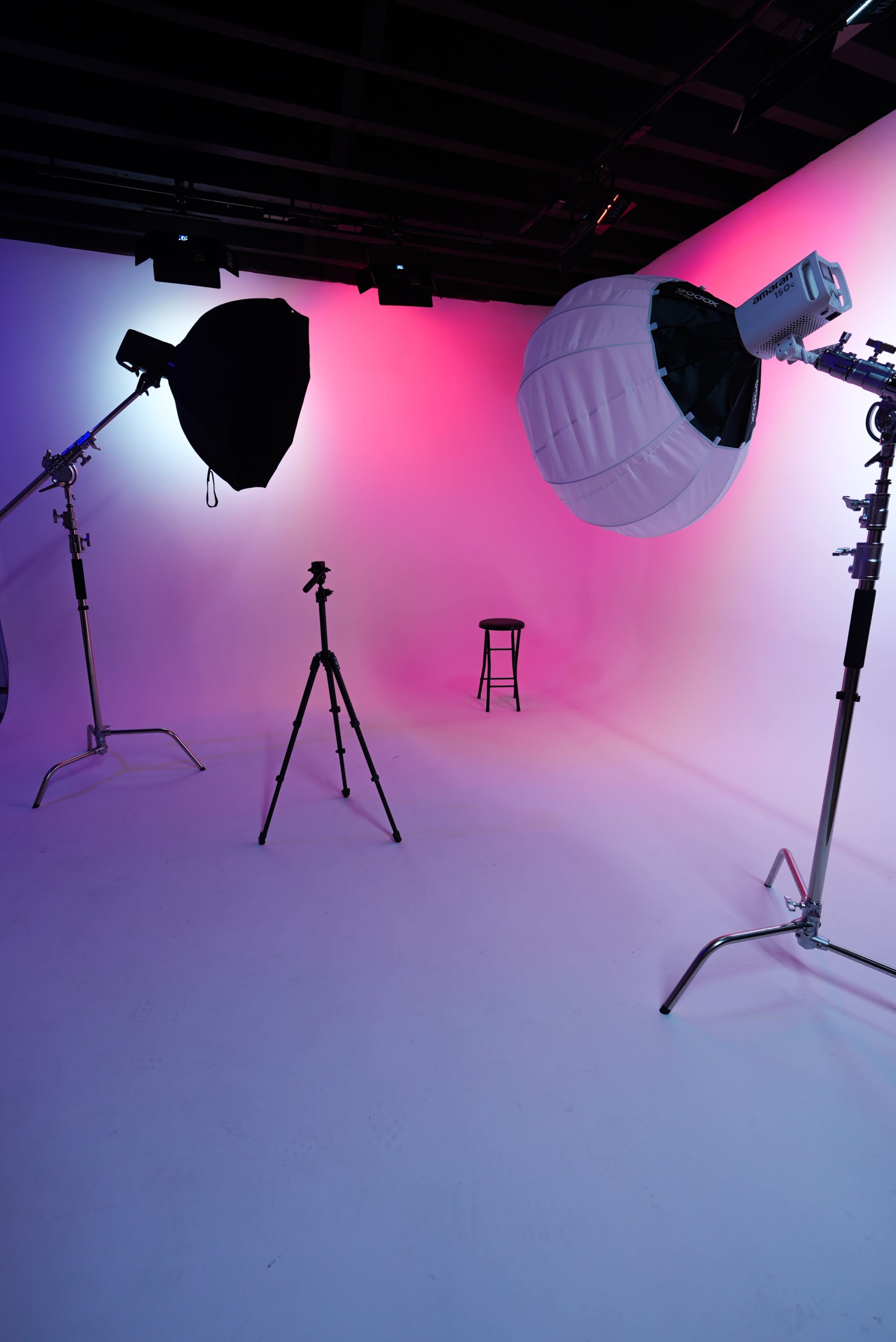 The image shows a photo studio with two light setups and a stool positioned on a seamless backdrop.