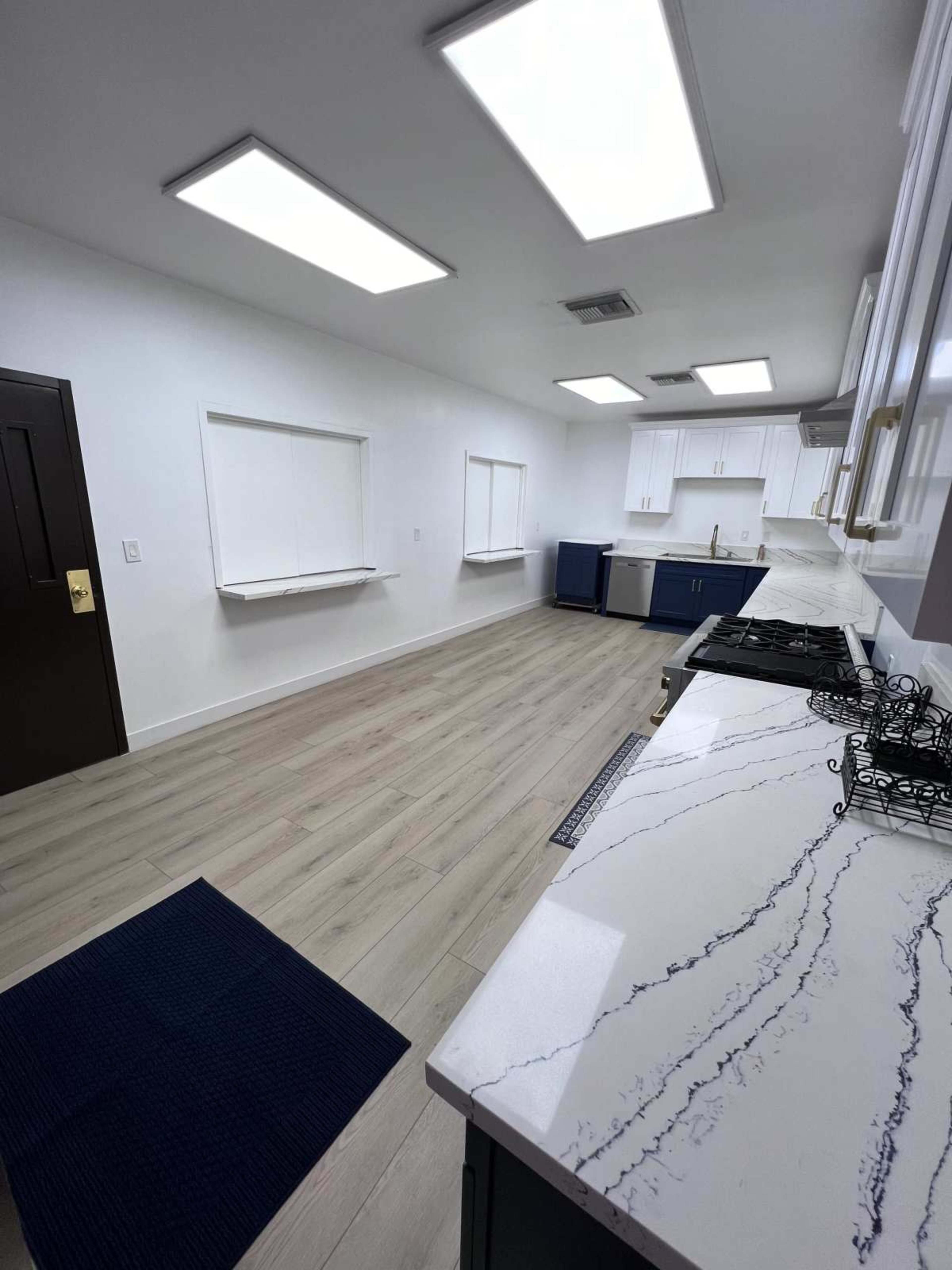 The image shows a modern kitchen with white cabinetry, marble countertops, and large skylights illuminating the space.