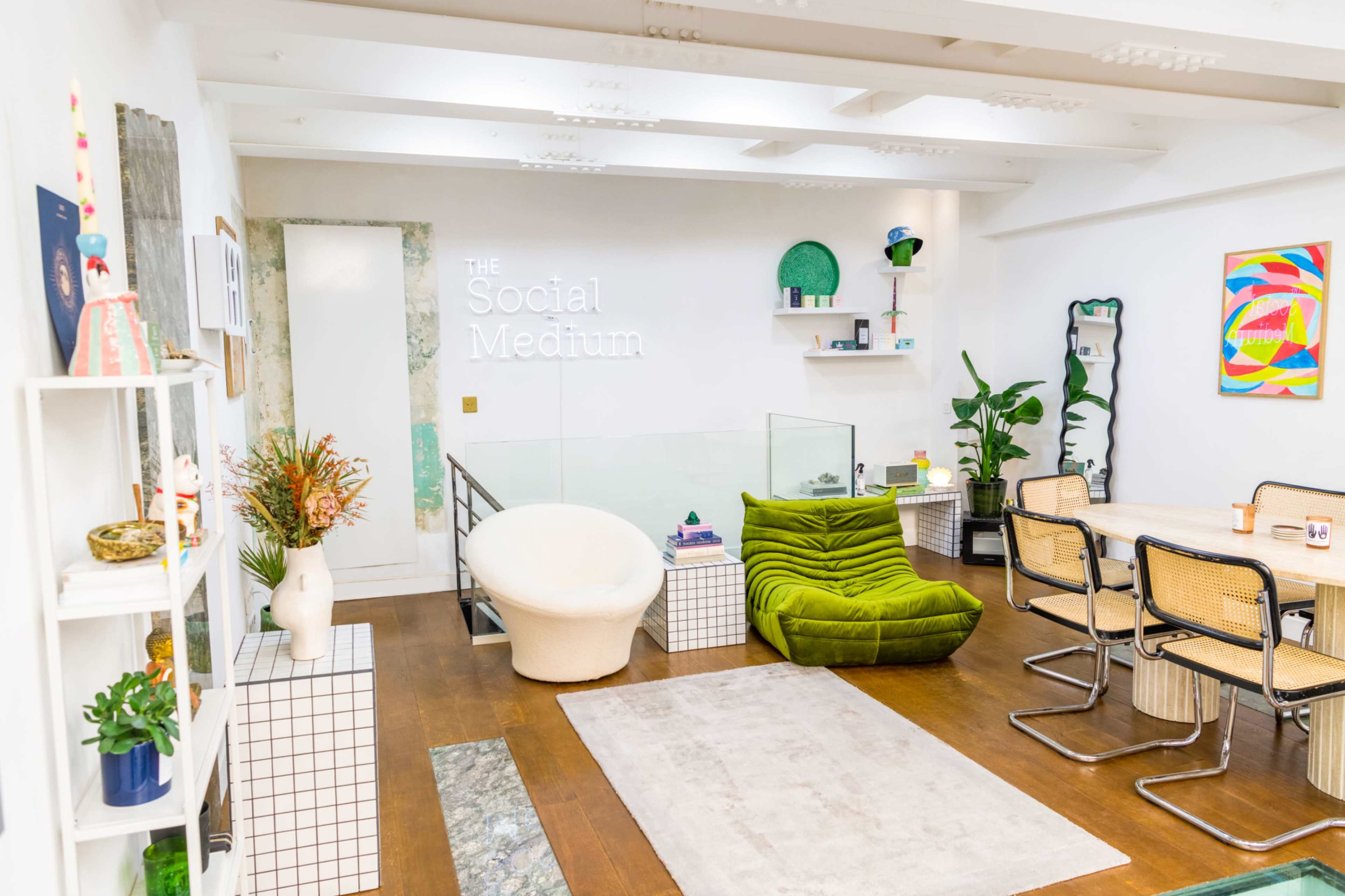 A modern interior space featuring a green lounge chair, a white swivel chair, a dining table with metal chairs, and various decorative elements on the walls and shelves.