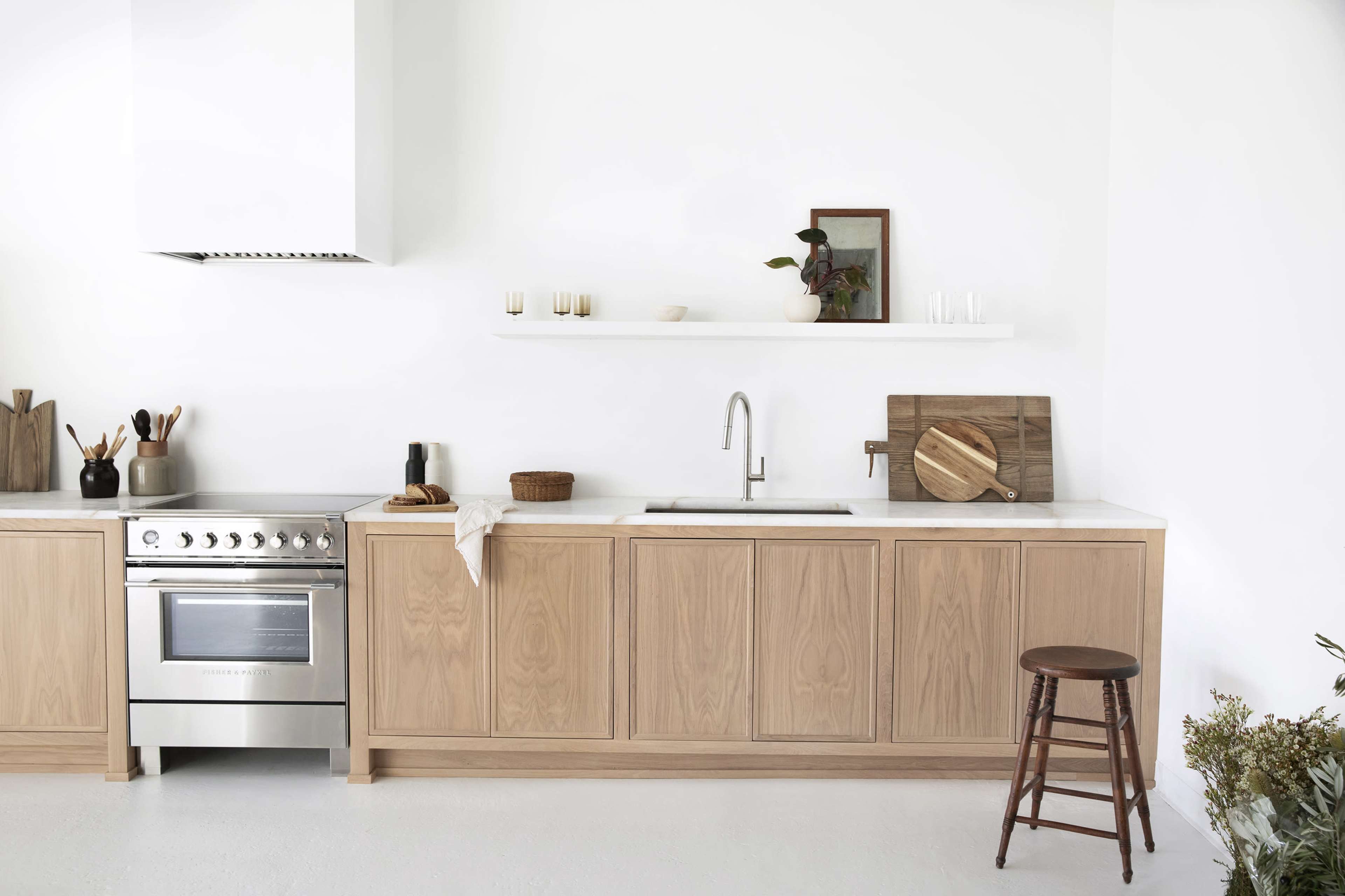 The image depicts a modern kitchen featuring wooden cabinetry, a stainless steel stove, and minimalistic decor on a white wall.