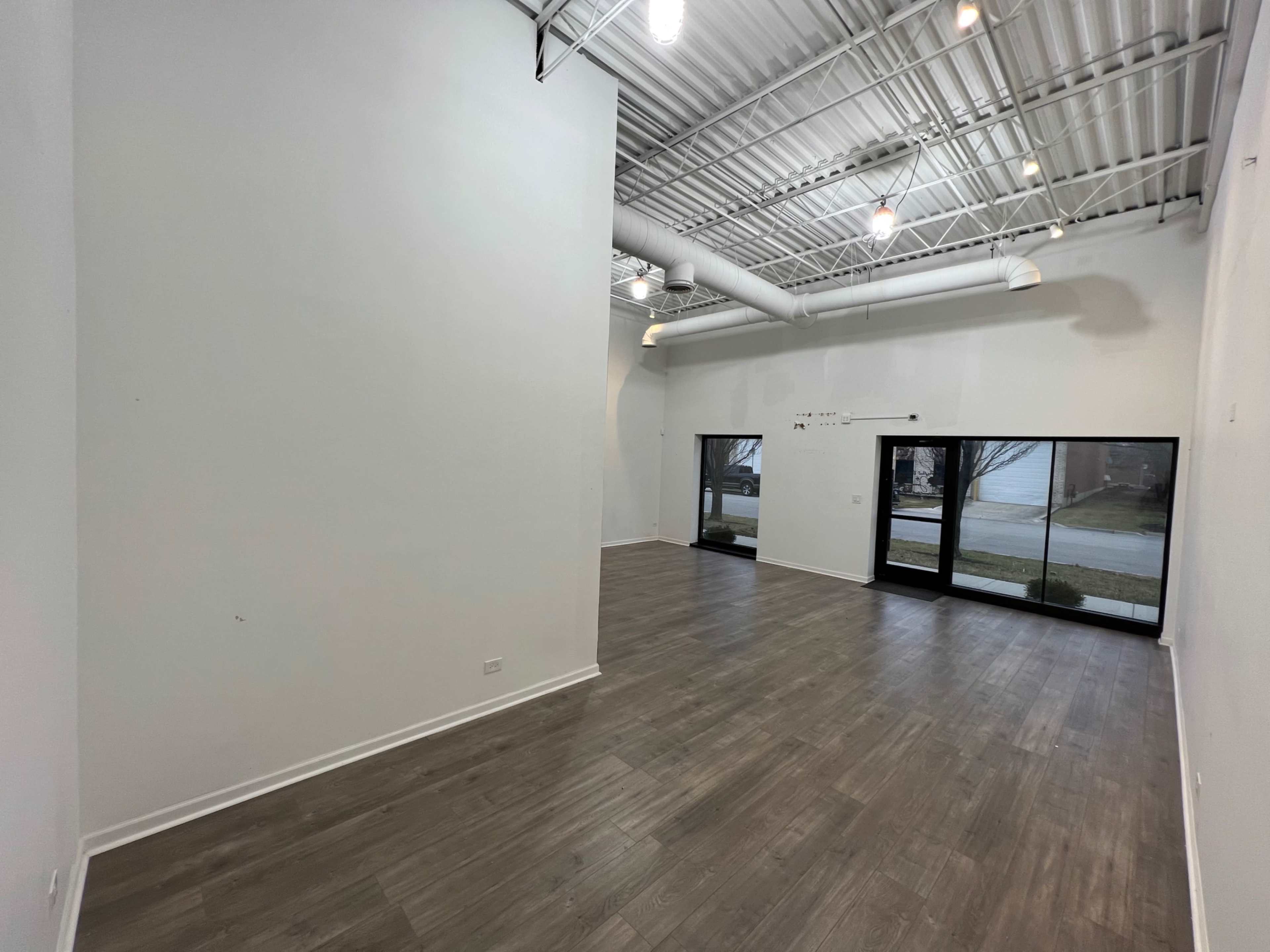 An empty indoor space with wooden flooring and large windows facing an exterior view.