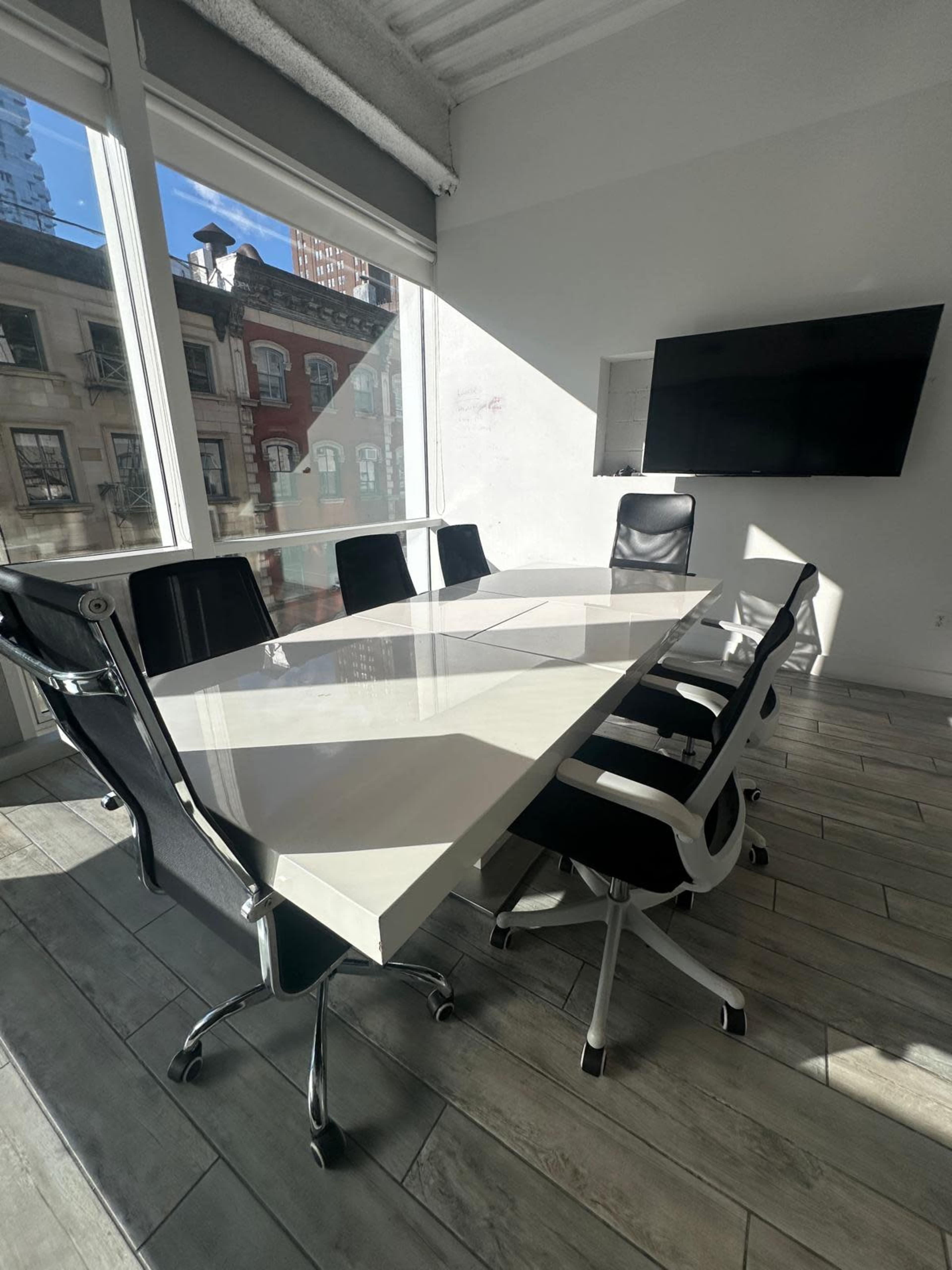 A modern conference room features a large white table surrounded by black and white ergonomic chairs, with large windows allowing natural light to fill the space.