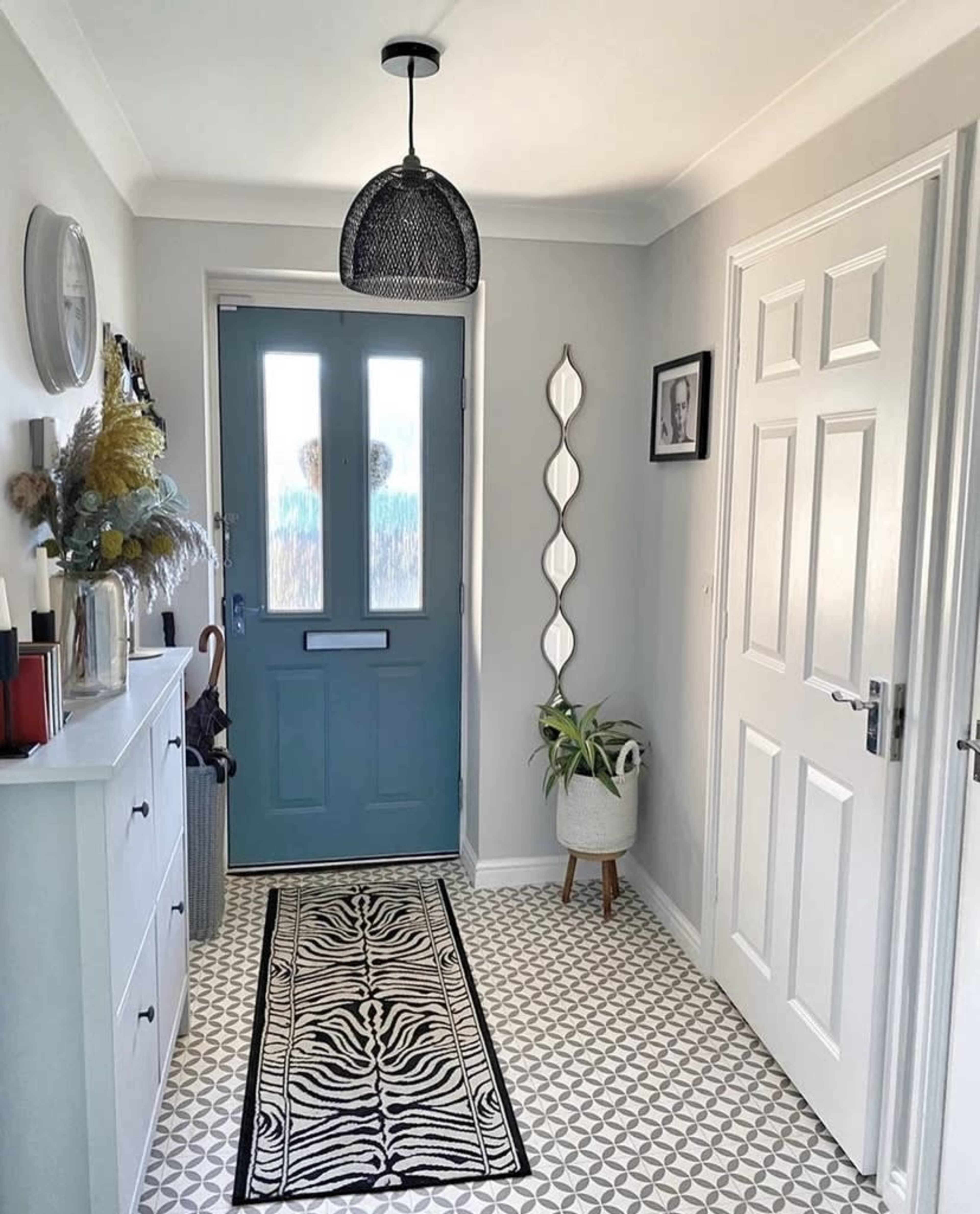 A bright hallway with a blue door, a patterned rug, a white cabinet, and a tall mirror on the wall.