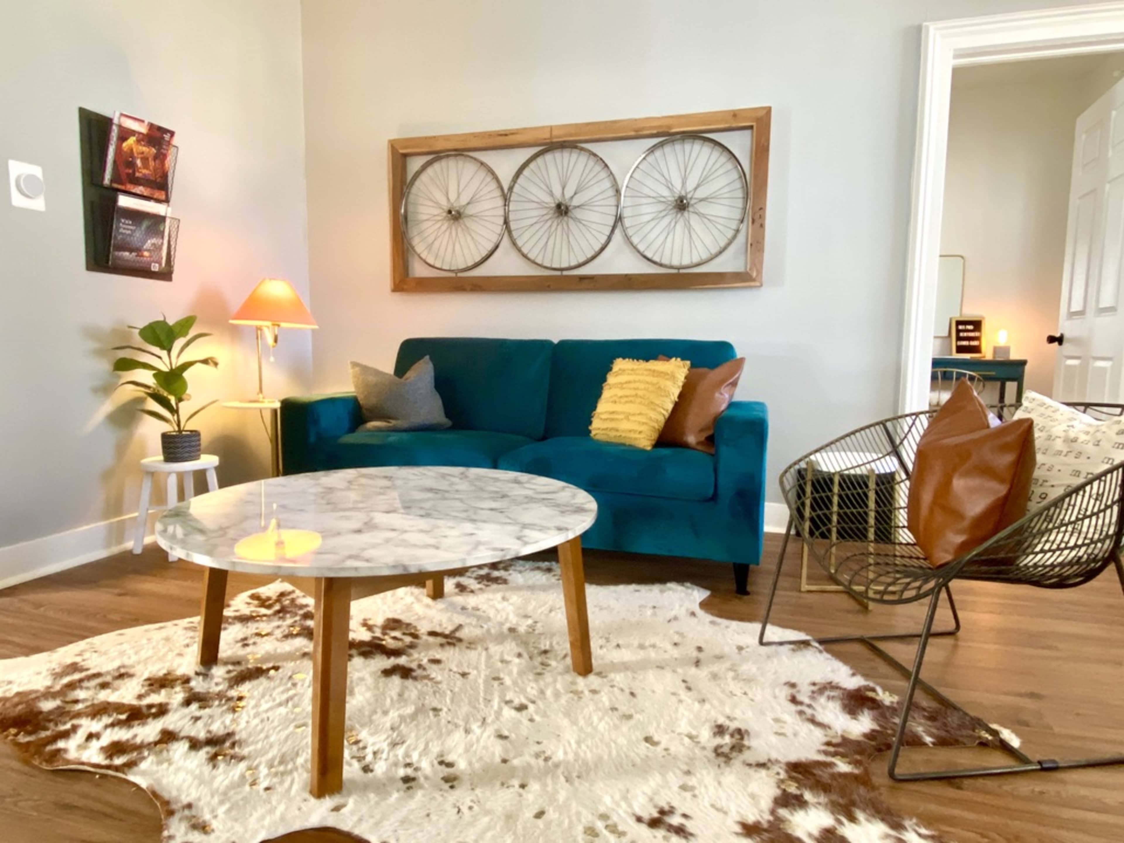 The scene features a cozy living room with a turquoise sofa, a marble coffee table, and decorative accents, including a plant and wall art.