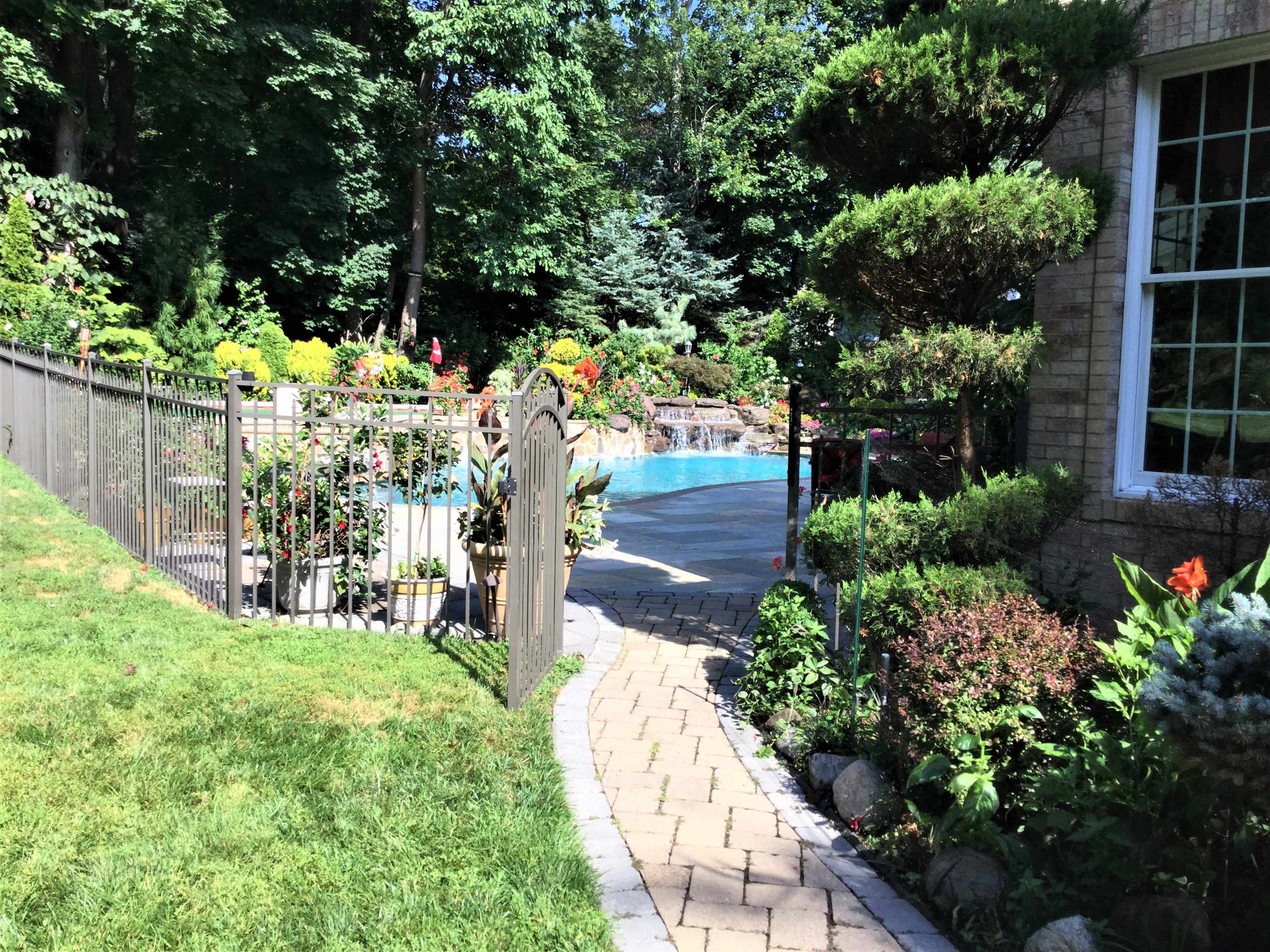 A garden path lined with flowers leads to a gated area around a swimming pool.