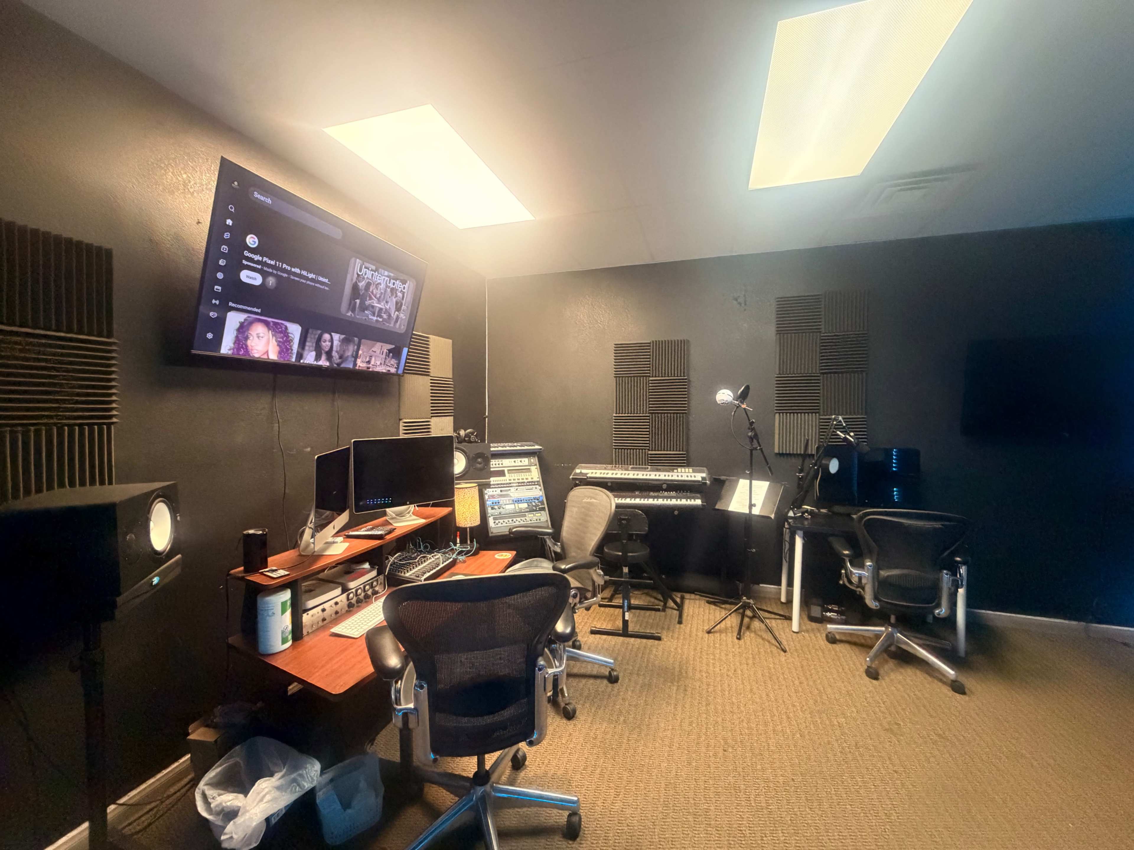 The image shows a music studio with wall-mounted displays, multiple audio equipment, and seating arrangements for recording or mixing tasks.