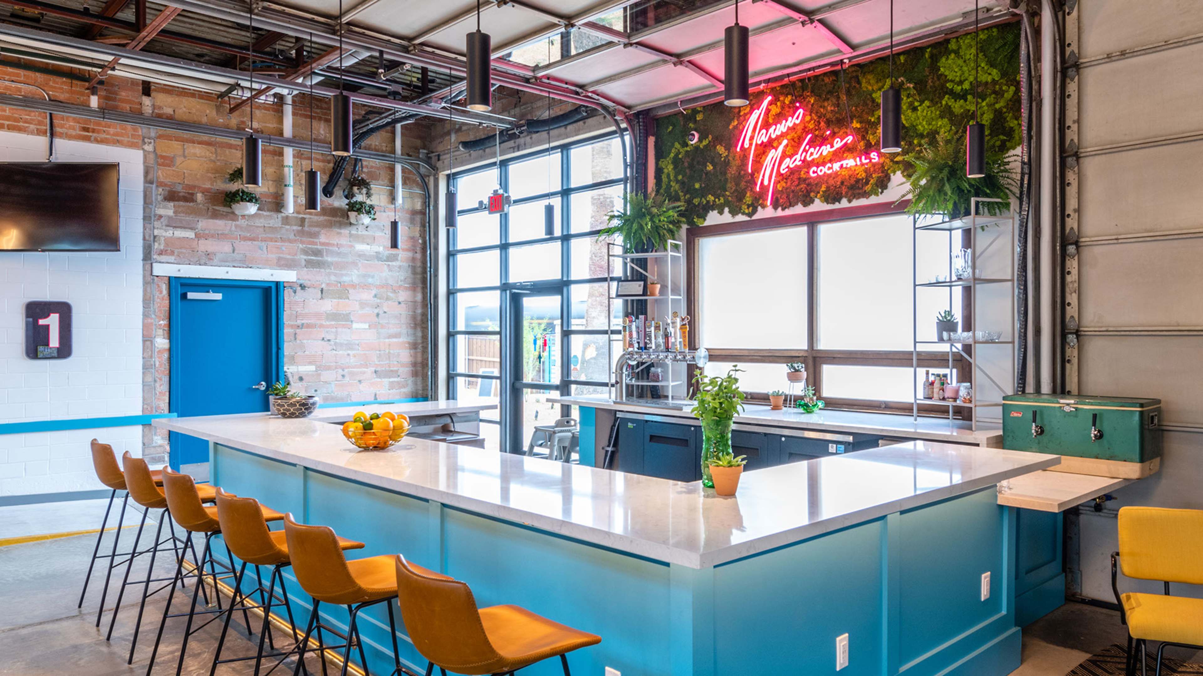A bright bar area features a light blue countertop with orange bar stools and a neon sign surrounded by greenery.