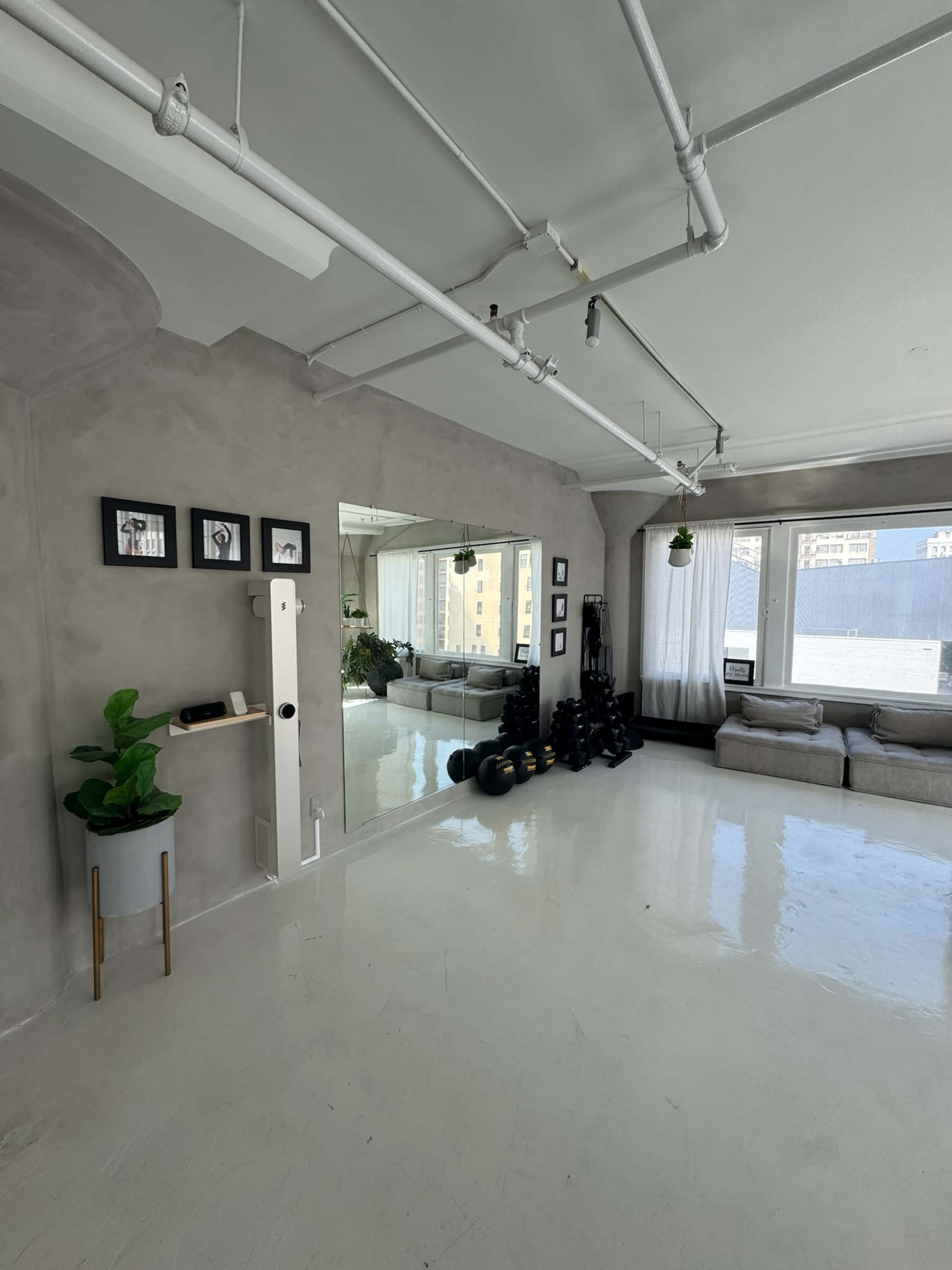 The image shows a spacious room with a polished white floor, featuring a large mirror, framed pictures on the wall, and exercise equipment neatly arranged in the corner.