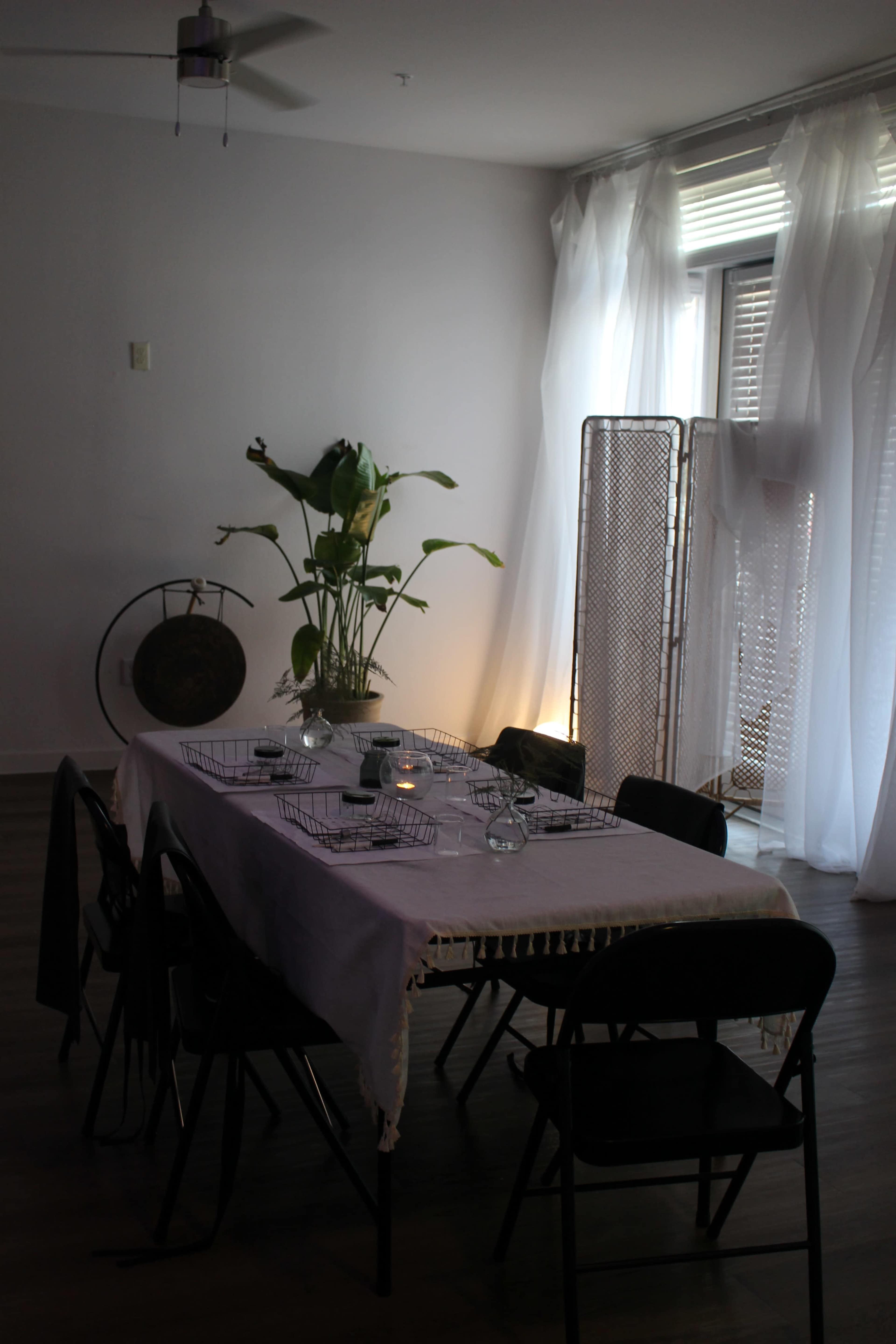 A dining table is set with chairs around it, and a plant centerpiece stands beside a decorative folding screen in a softly lit room.
