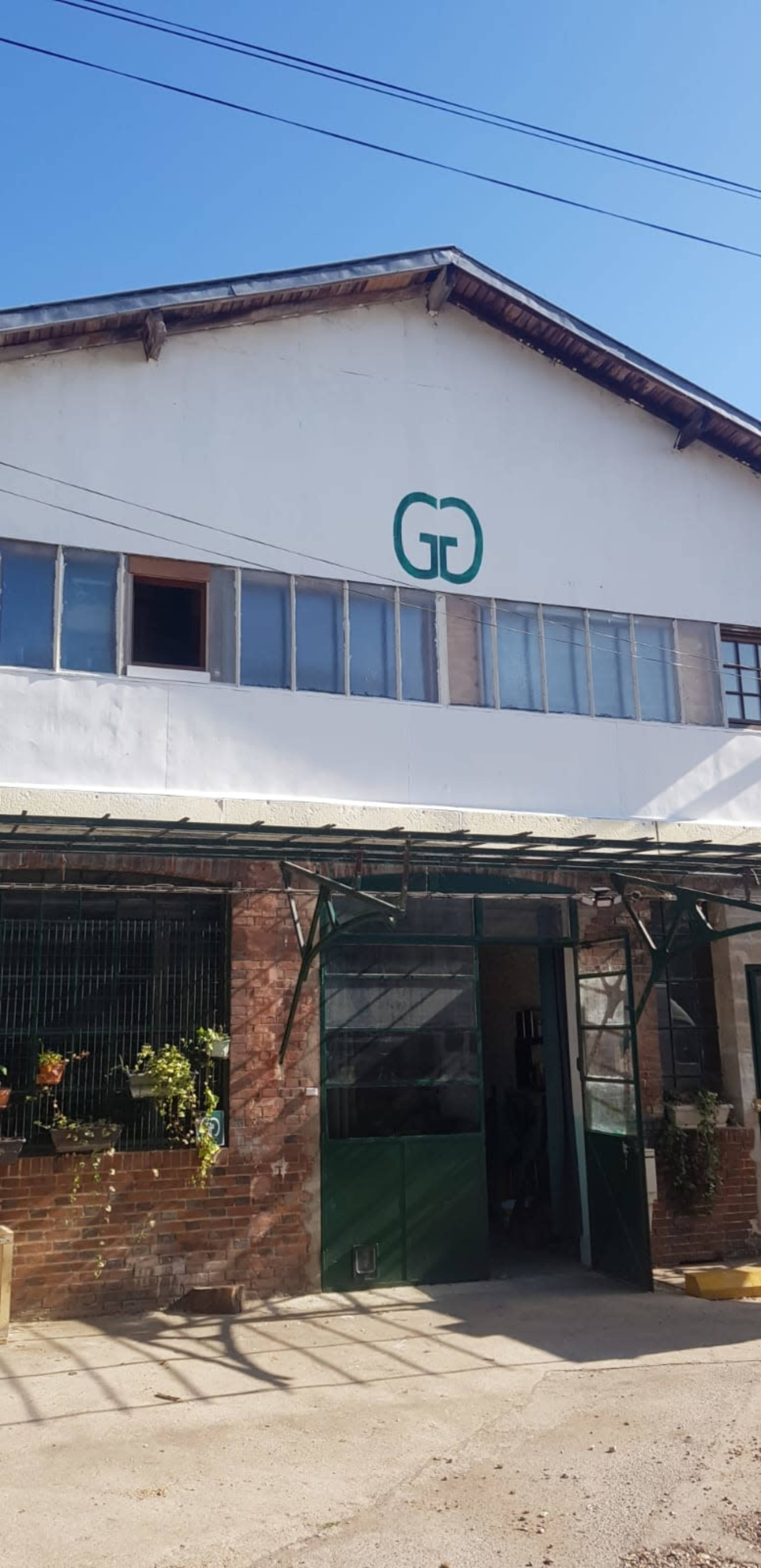 The image shows a brick building with large windows and a green entrance, featuring a logo of interlocking letters "G" and "D" on the facade.