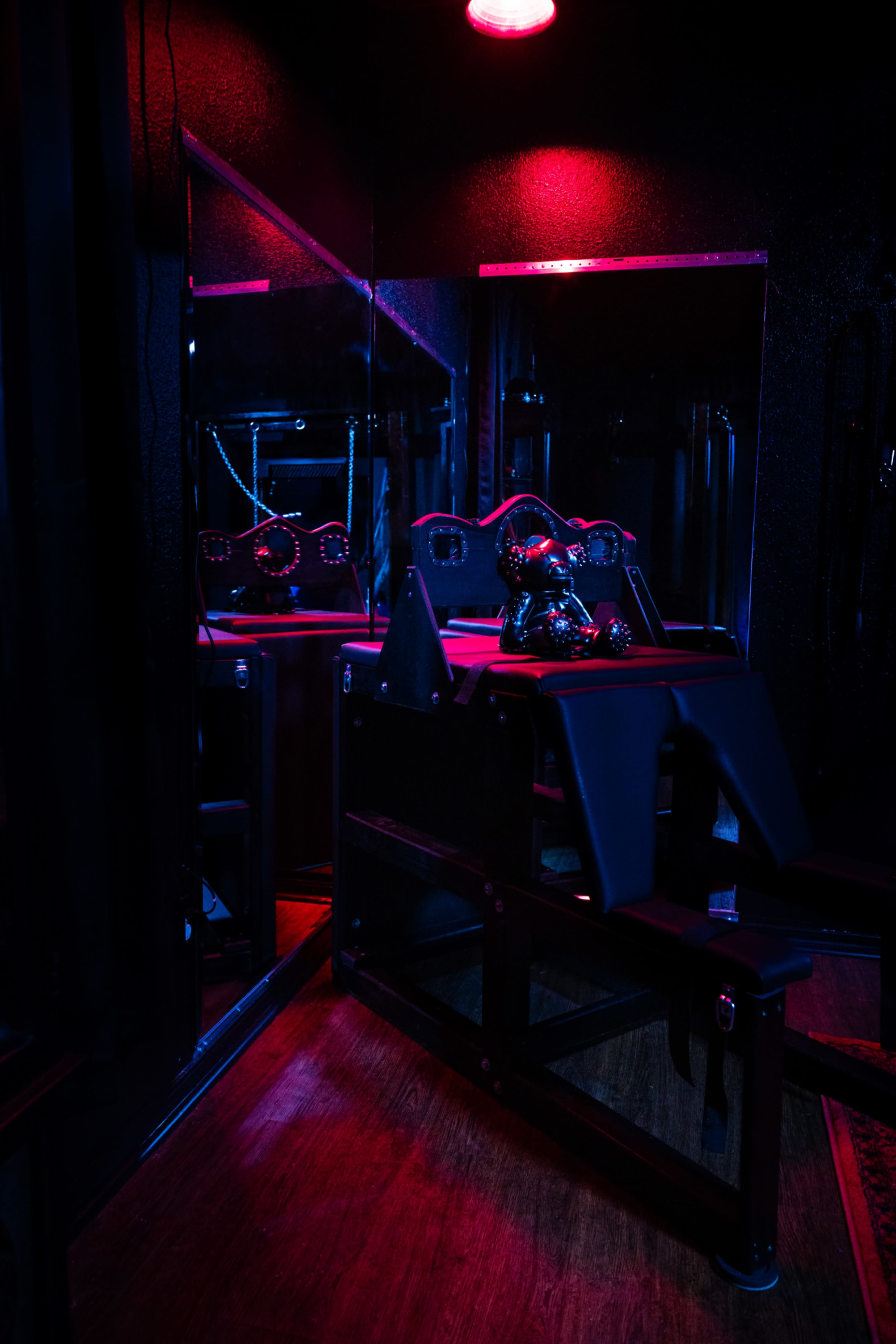 The image shows a dimly lit room with a mirror reflecting a training machine and a seated figure covered in a black cloth.