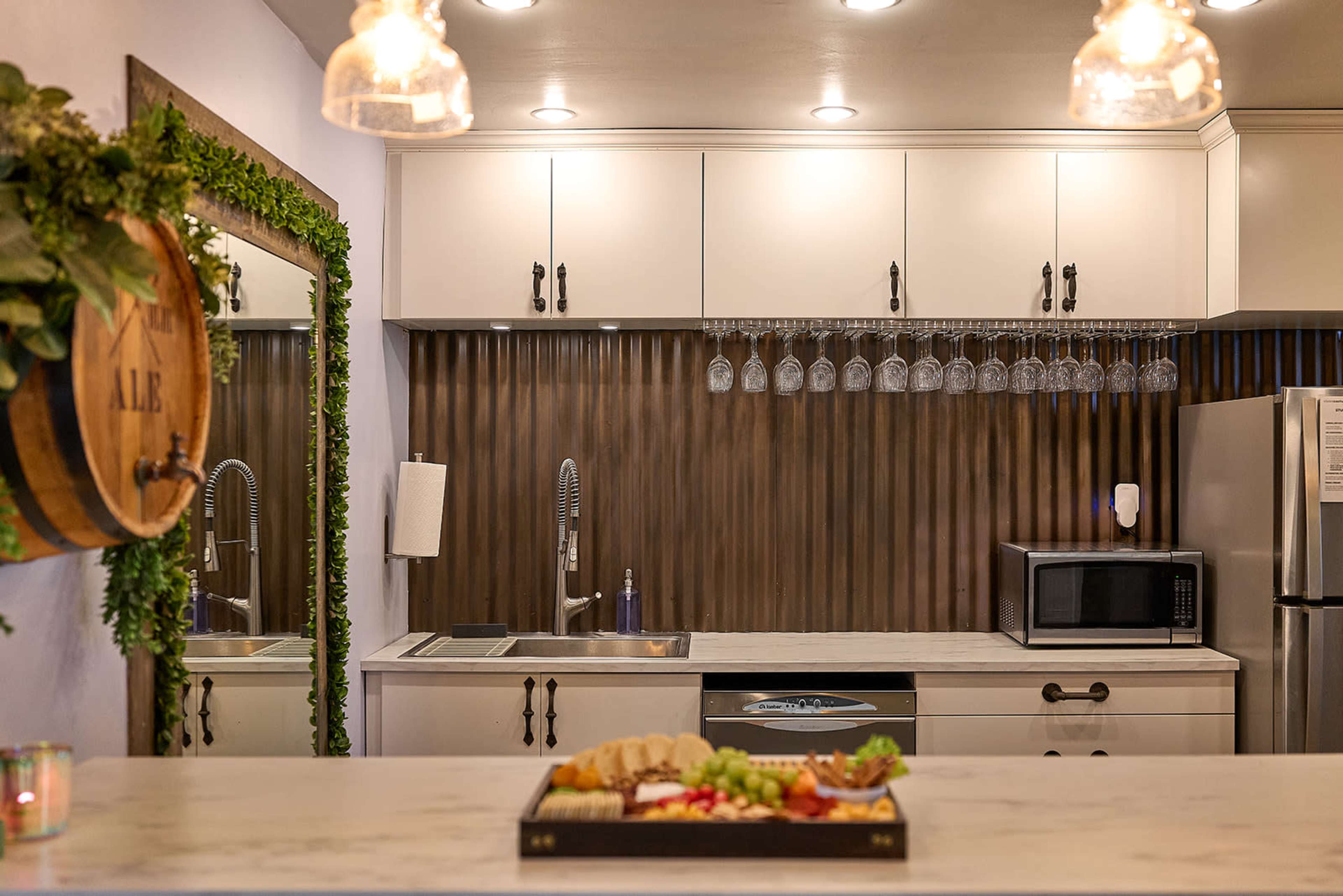 The image shows a modern kitchen with a wooden accent wall, a countertop featuring a charcuterie board, and various kitchen appliances including a microwave and a refrigerator.
