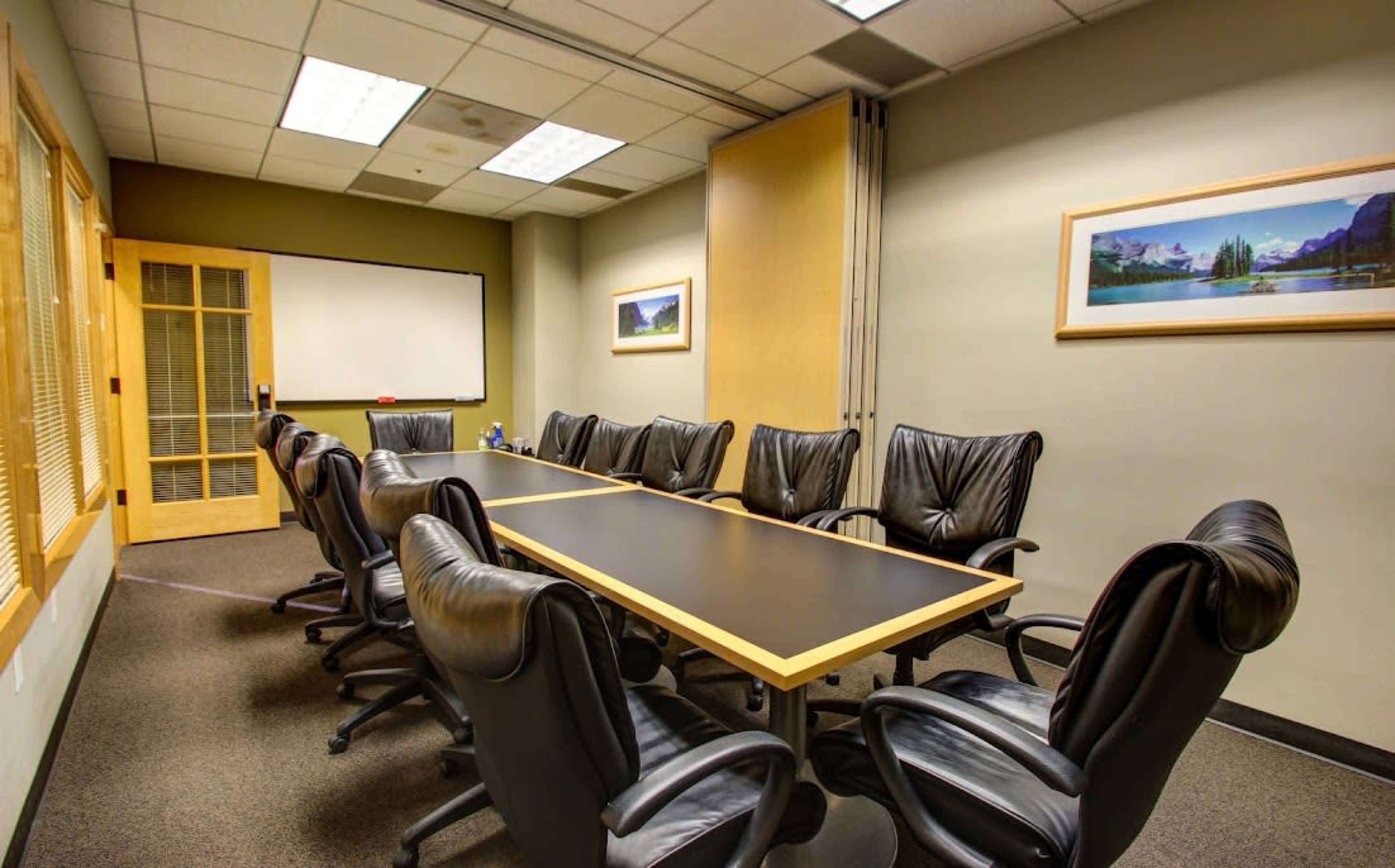 A conference room with a long table surrounded by black leather chairs and a whiteboard on one wall.