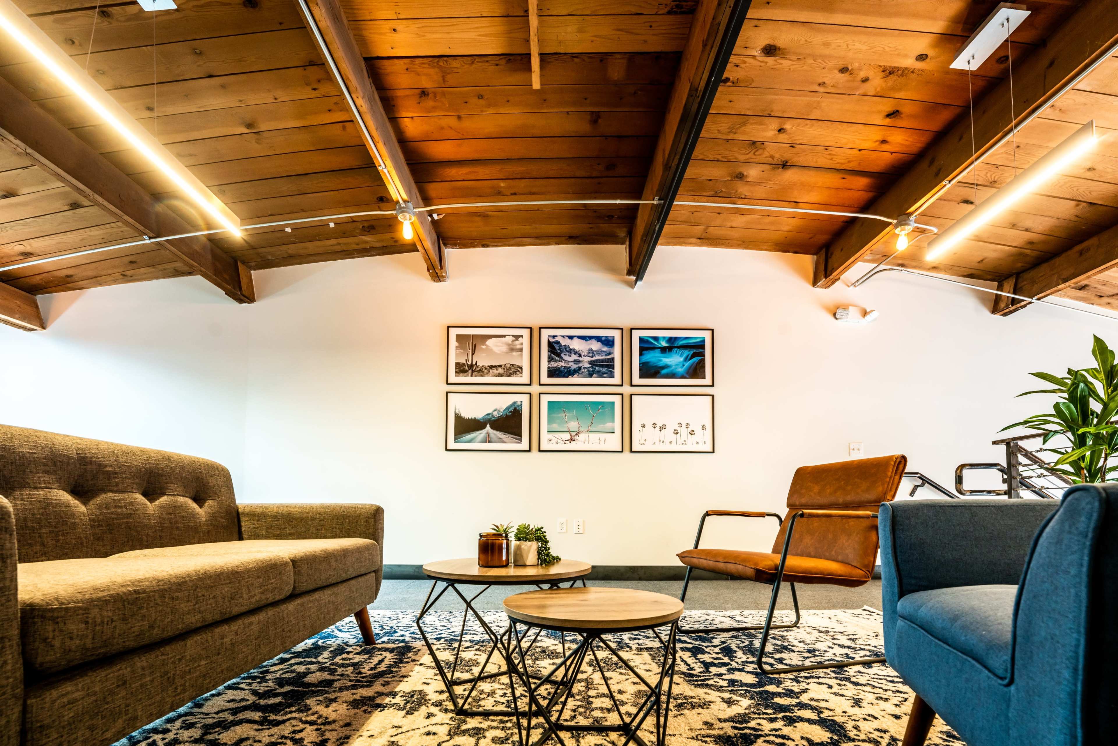 A well-lit living space featuring a wooden beam ceiling, two sofas, a round coffee table, and framed photographs on the wall.