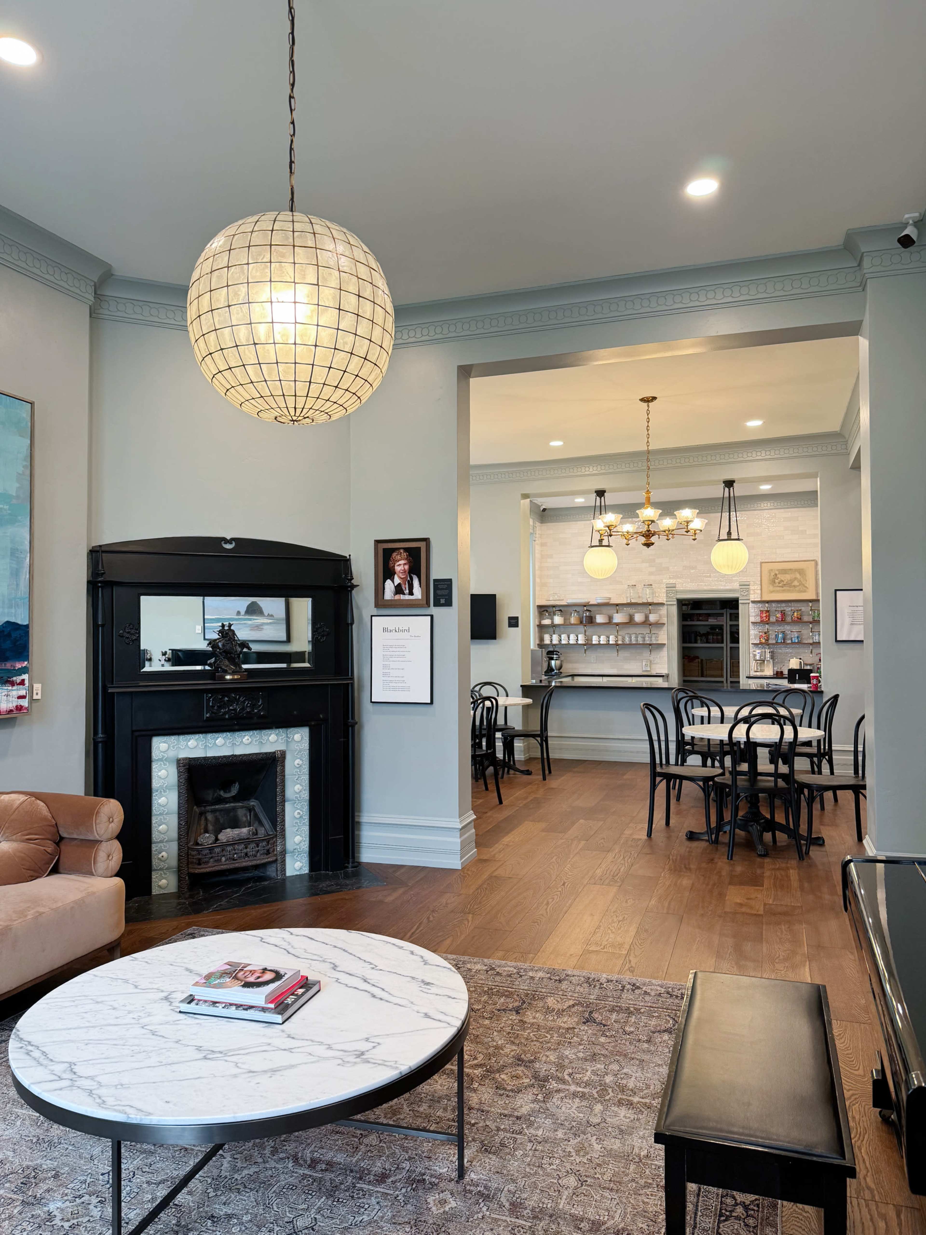 A cozy cafe interior featuring a marble coffee table, a fireplace, and a counter with chairs and tables against a light-colored wall.