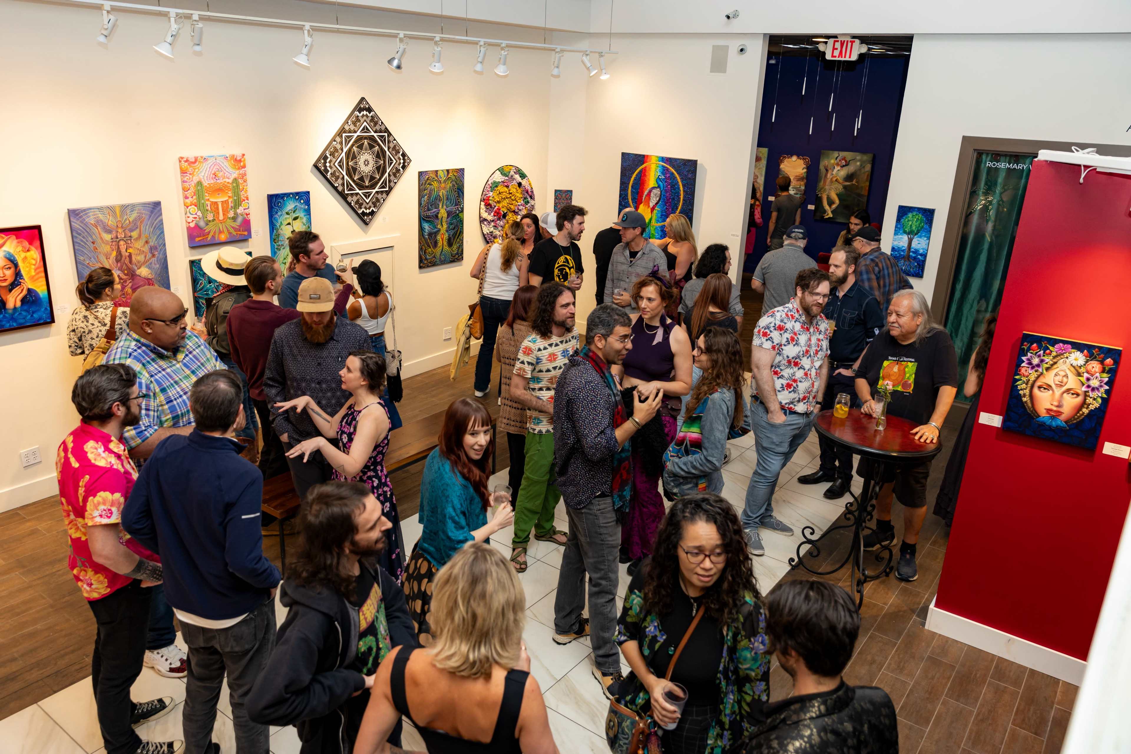 A diverse group of people gathers in an art gallery filled with colorful paintings on the walls.