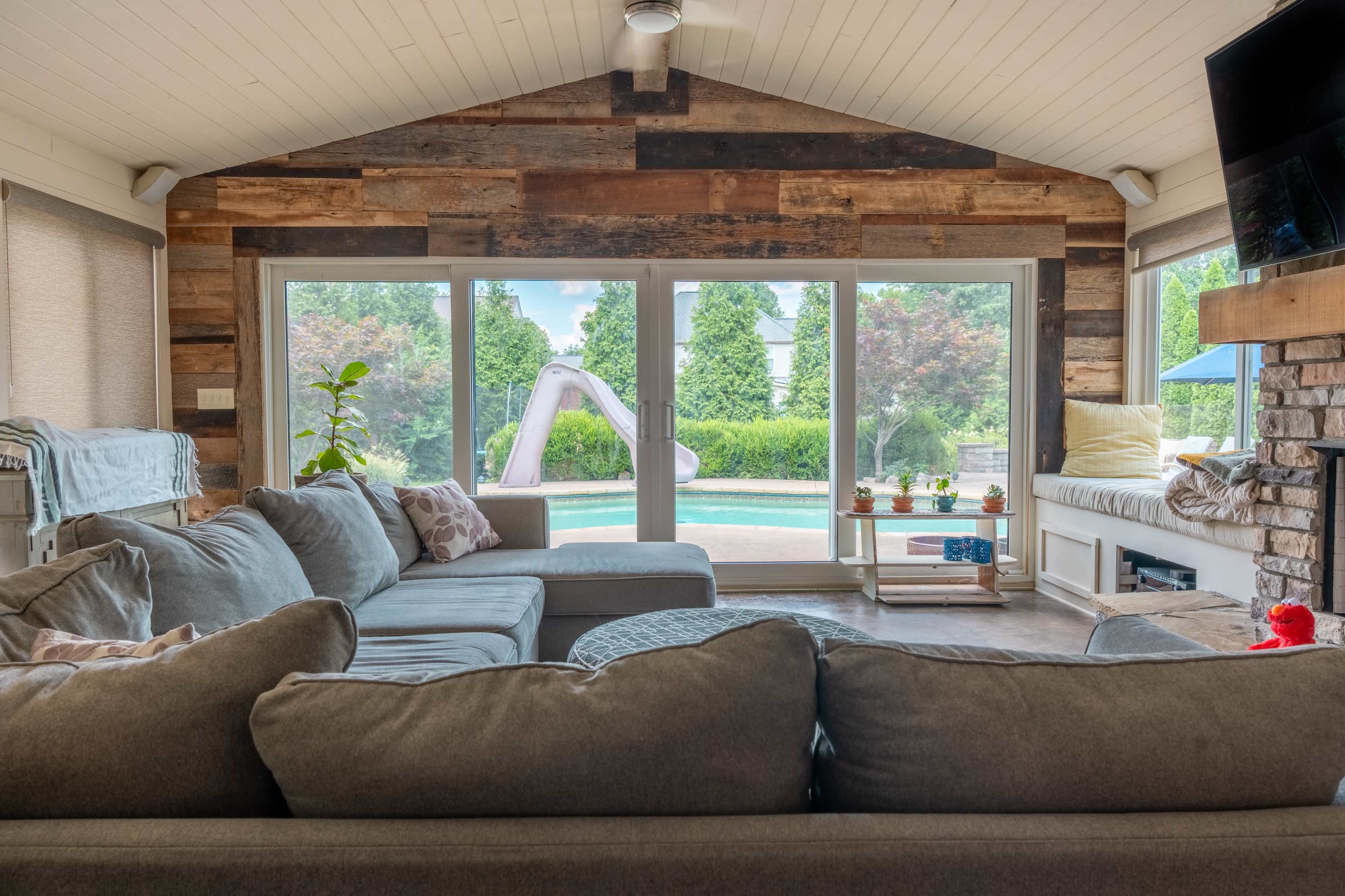A living room features a large sectional sofa facing sliding glass doors that open to a pool area with a slide.