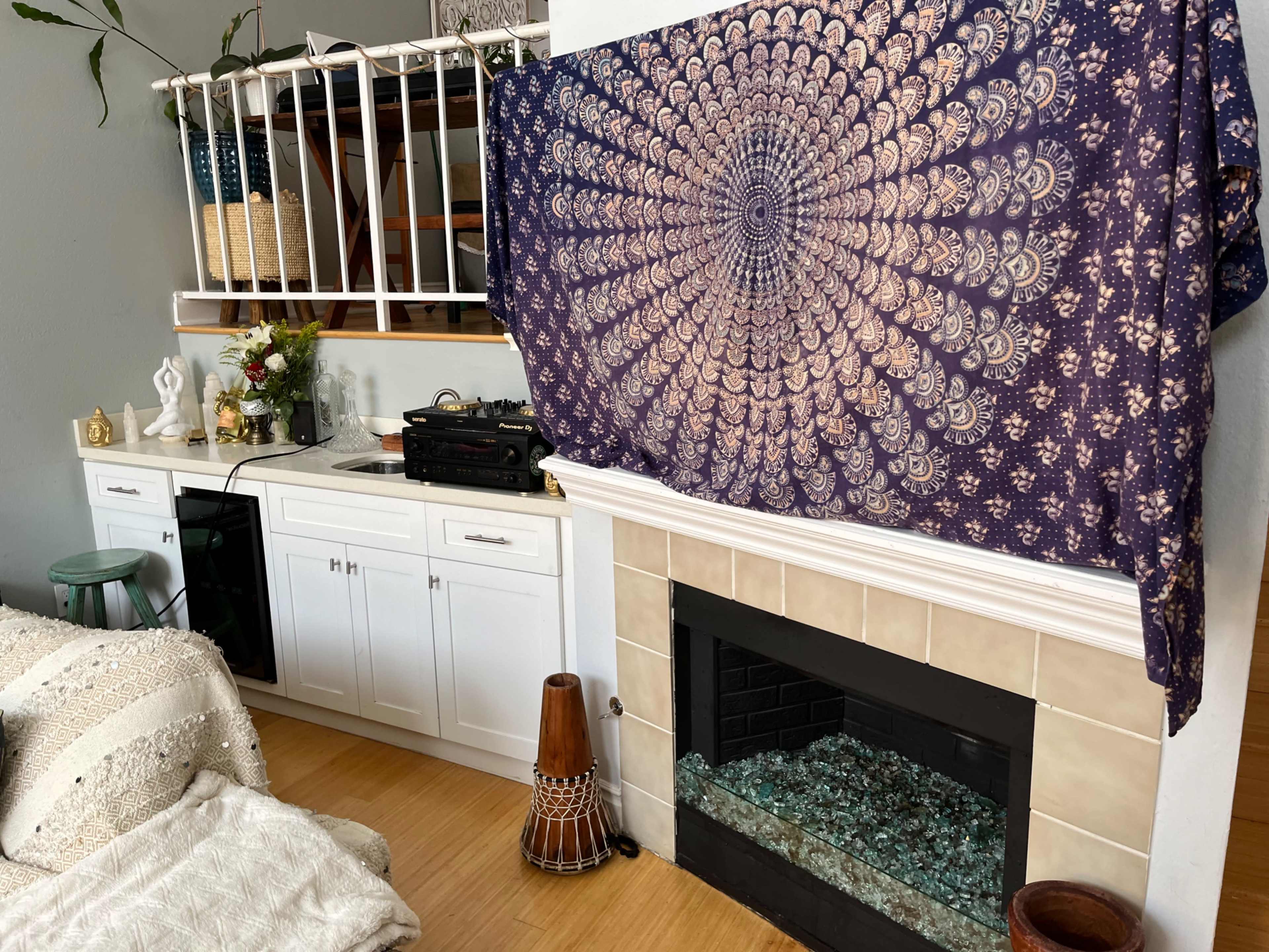A cozy living space featuring a white cabinet, a fireplace with glass stones, and a wall adorned with a patterned tapestry.