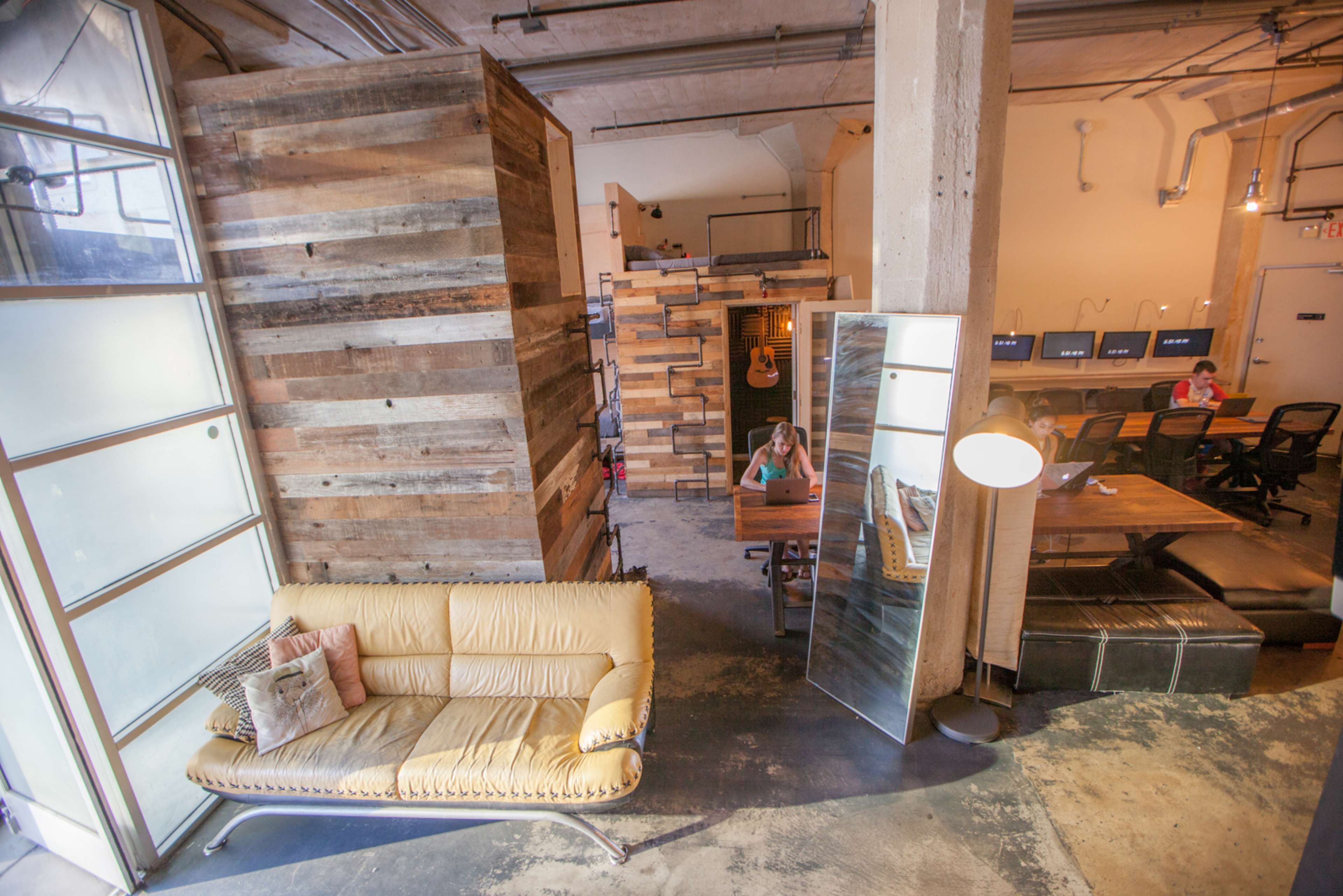 A spacious office interior with wooden partition walls, a yellow couch, a mirror, and workstations in the background.