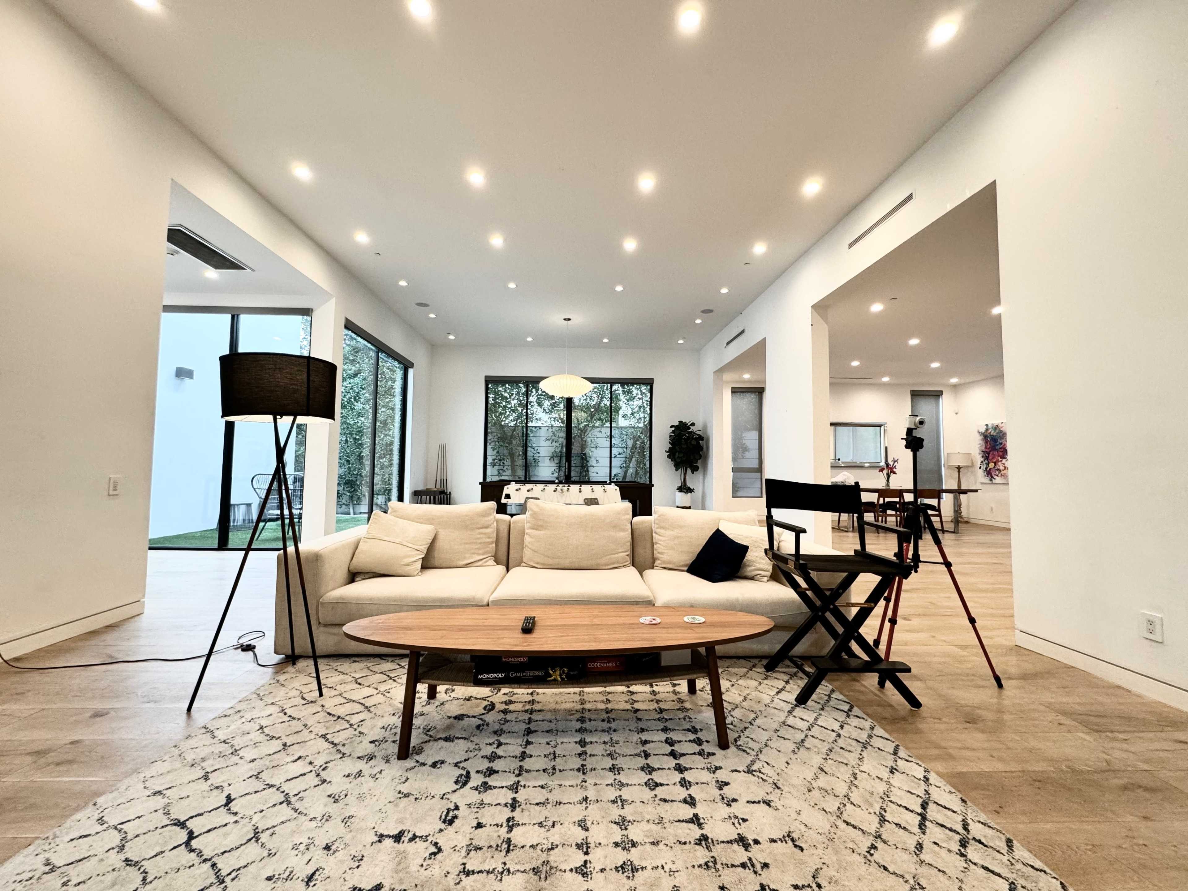 A modern, open-concept living space featuring a light-colored sofa, a round coffee table, and large windows that offer a view of the outdoors.