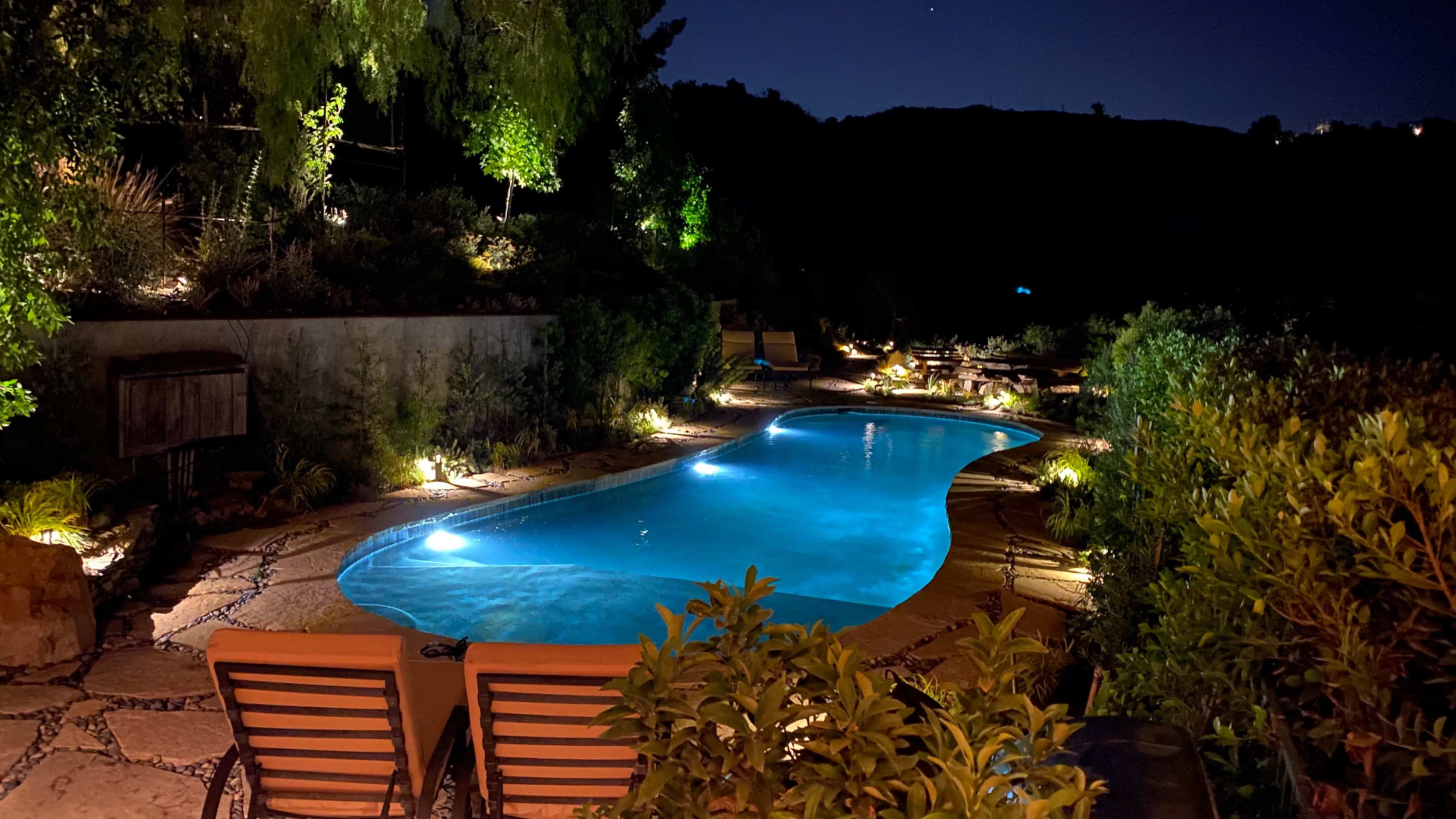 A pool surrounded by landscaped greenery and softly lit seating areas is visible at night.
