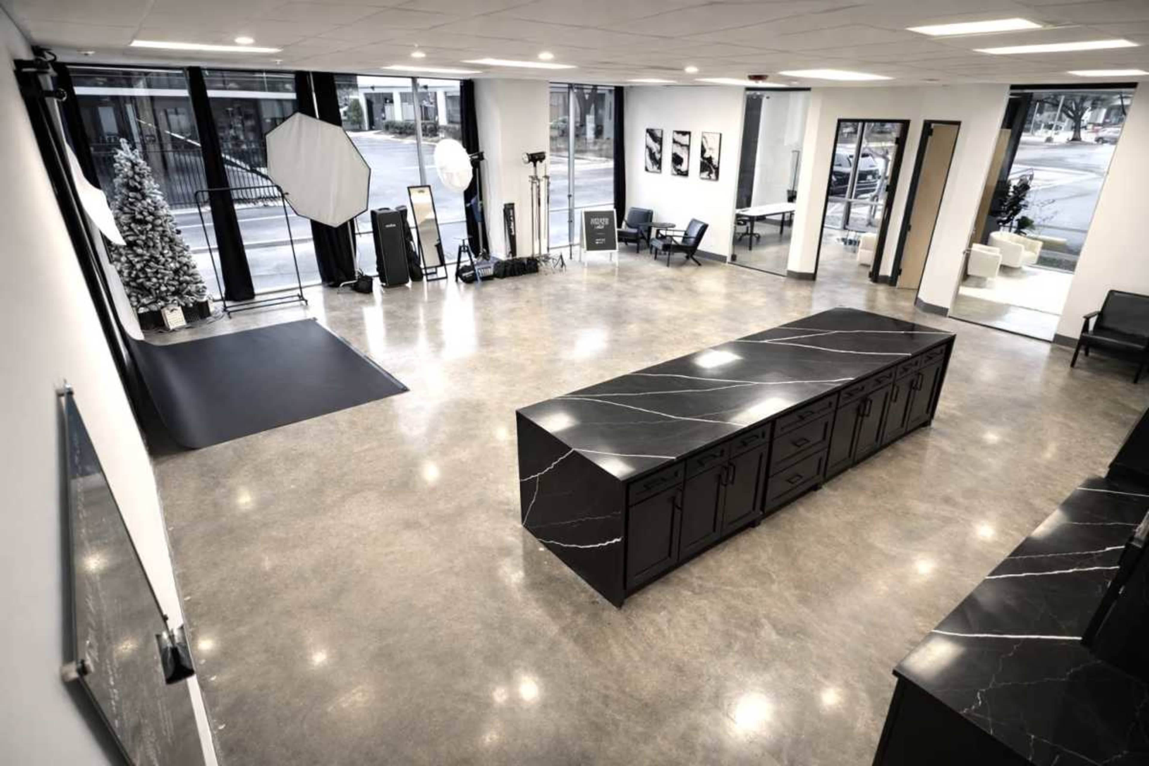 A modern studio features polished concrete floors, a large black marble countertop, and various photography equipment arranged in an open space with large windows.